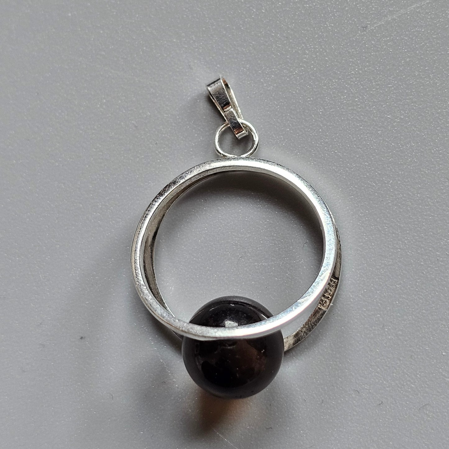 Silver circular pendant with a dark spherical bead.