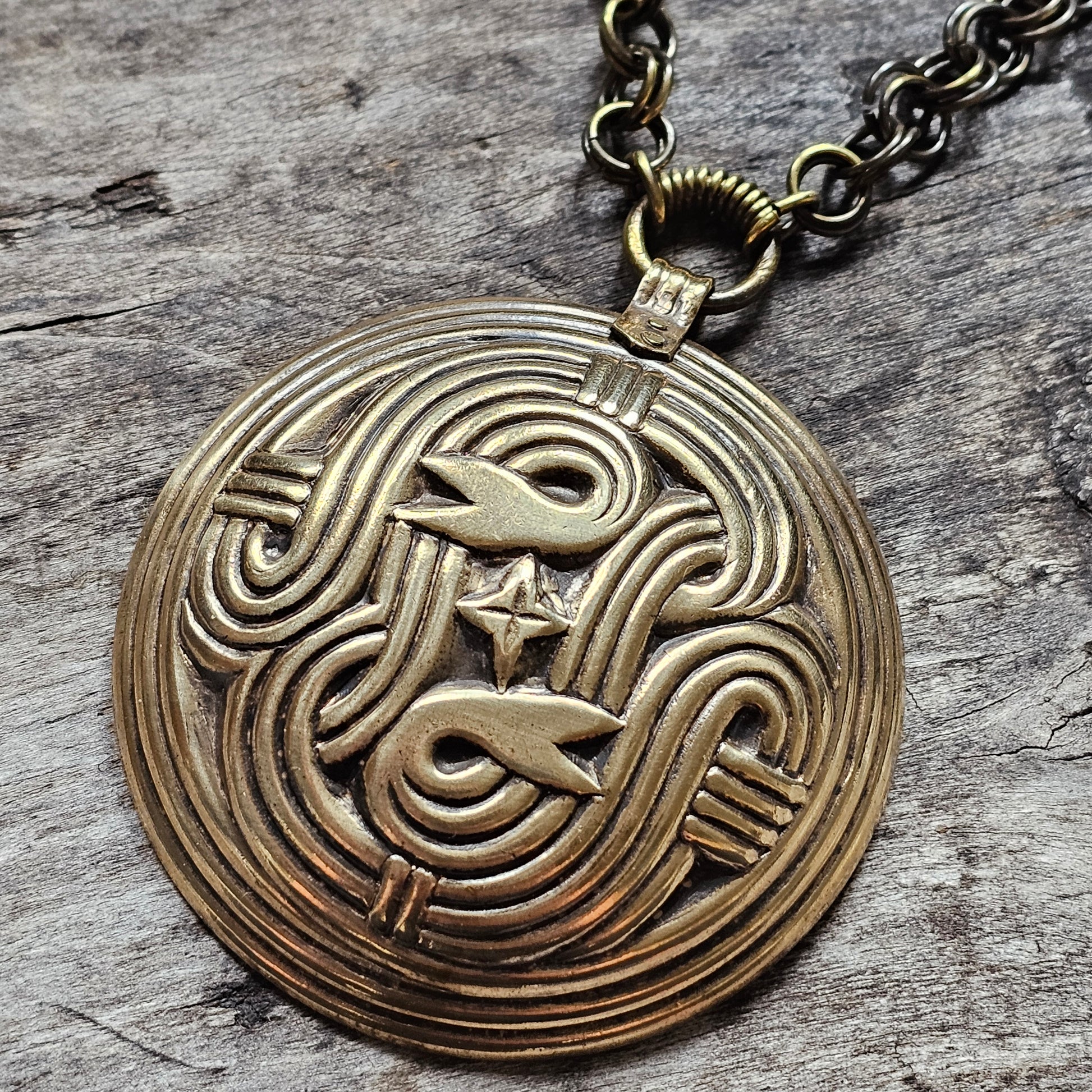 Circular bronze pendant with an intricate, maze-like design featuring stylized fish motifs.