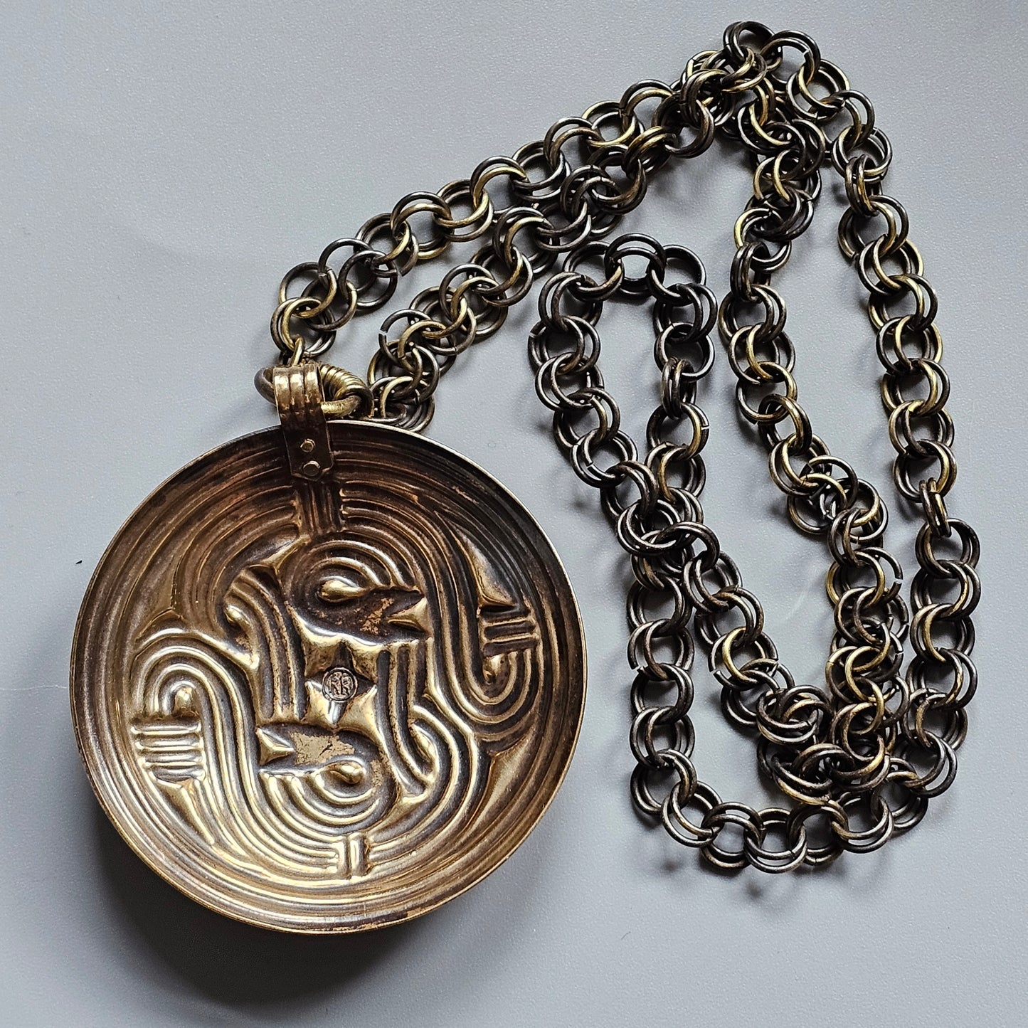 Circular pendant with an intricate maze-like pattern attached to a metal chain necklace.