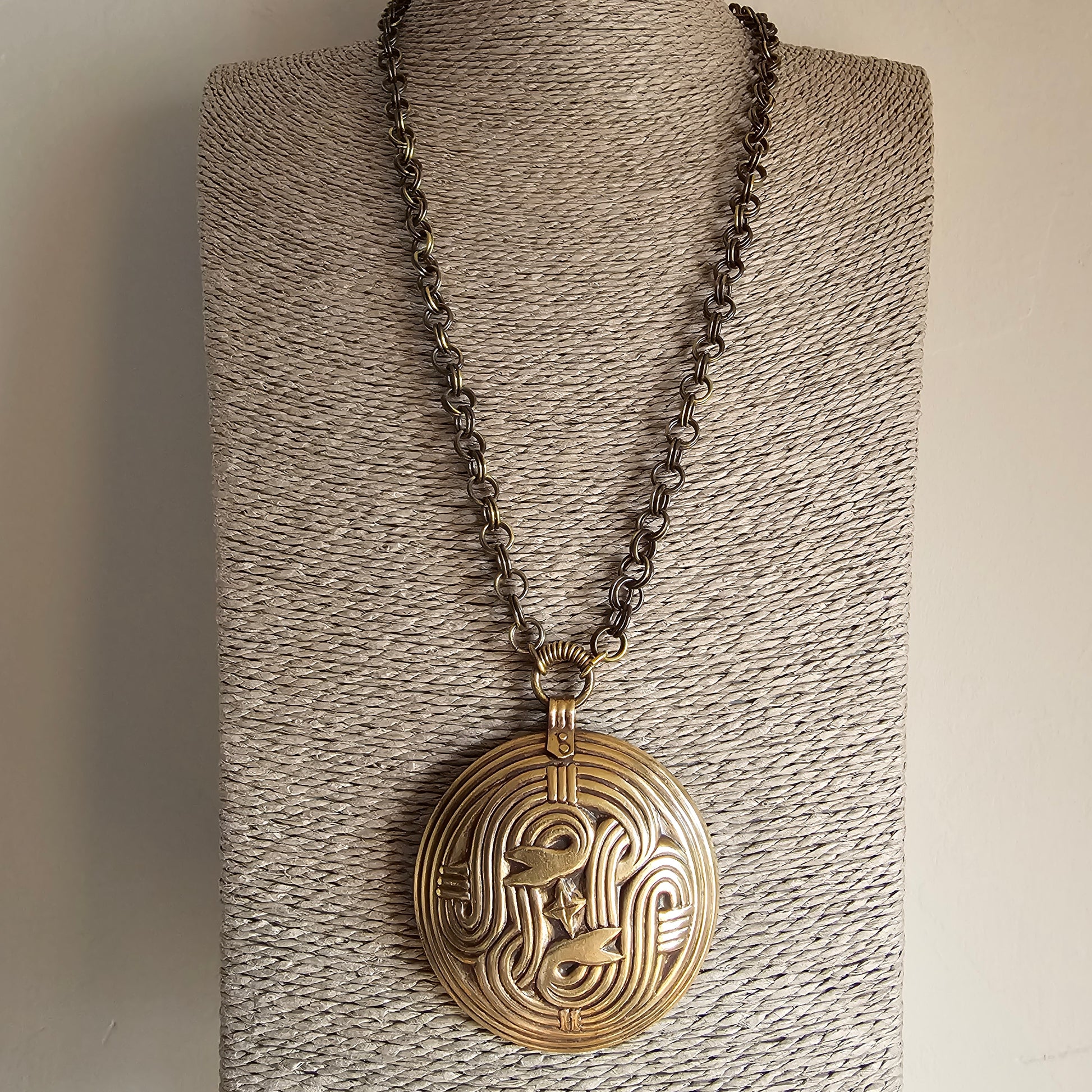 Circular gold pendant with an intricate face design hanging from a chain necklace.