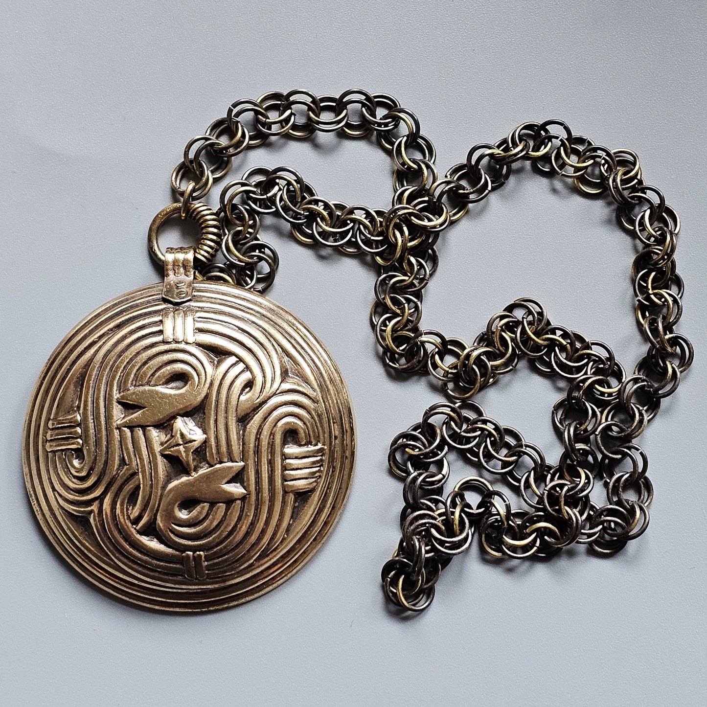 Gold medallion pendant with an intricate swirling design on a silver chain necklace.