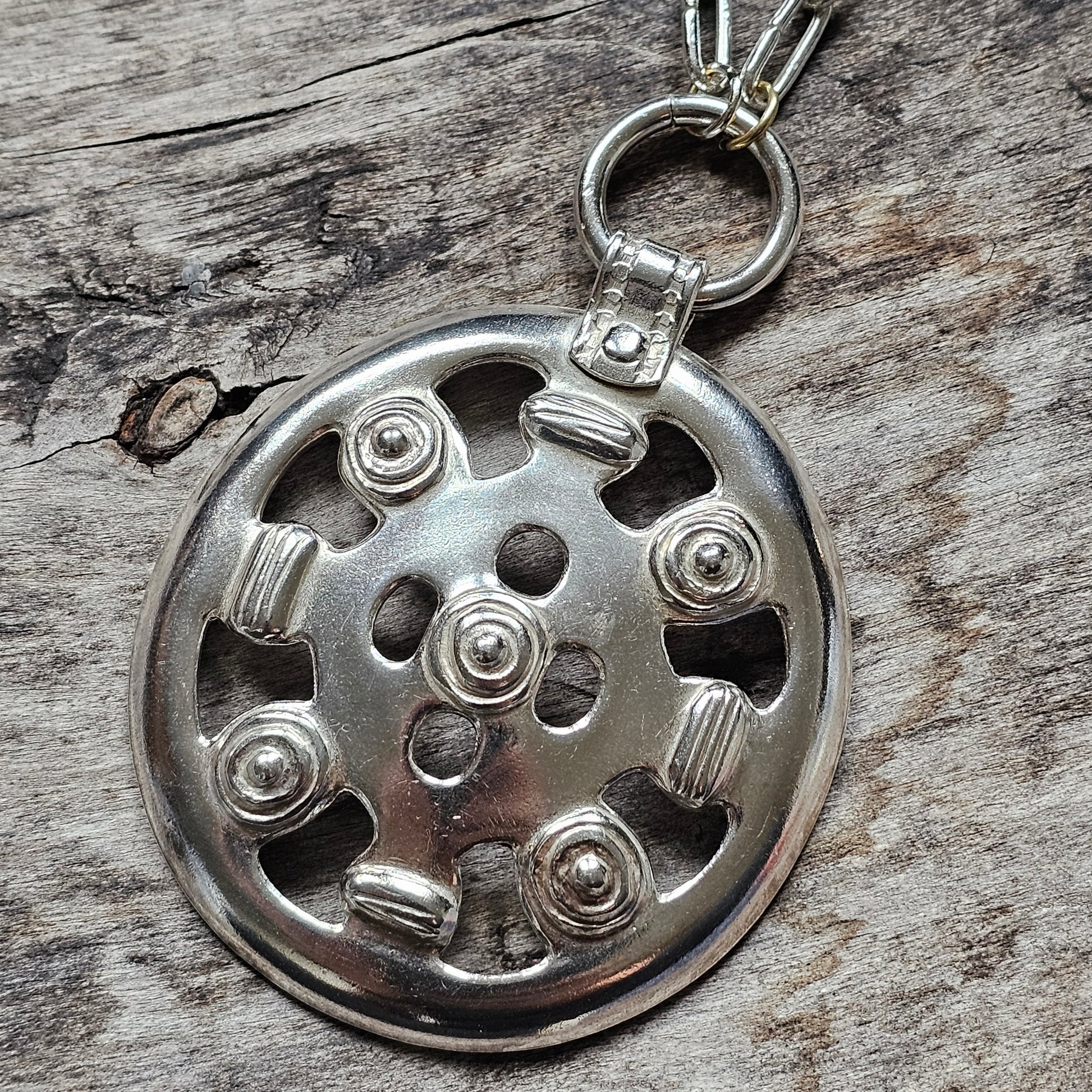 Metal keychain or pendant with a circular design featuring rivets and cutouts.