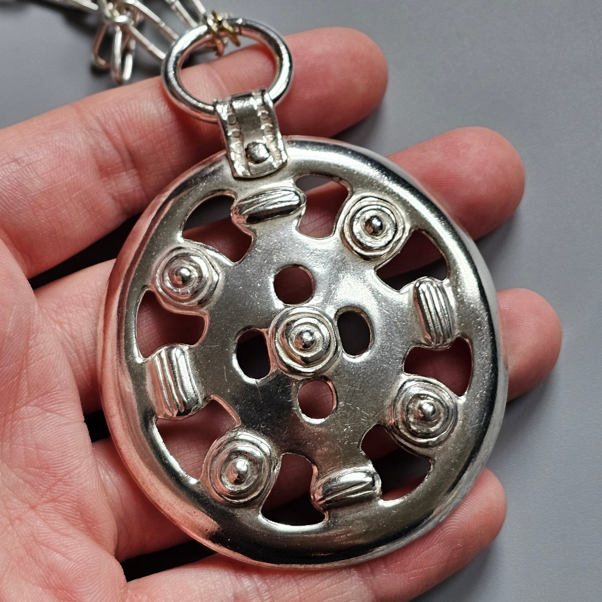 Circular metal pendant with decorative cutouts and raised elements resembling a wheel design.