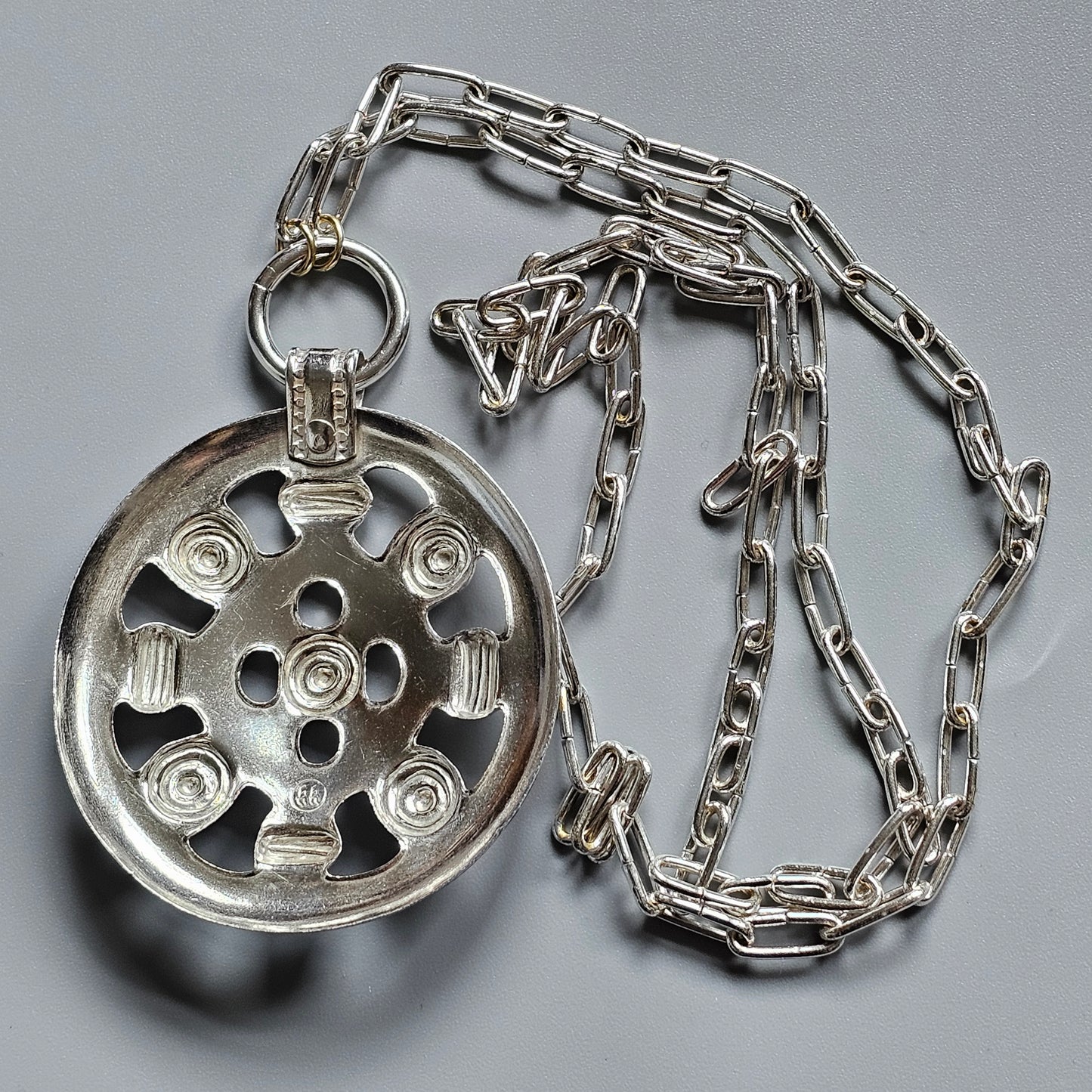 Silver pendant necklace featuring a circular wheel-like design on a chain.