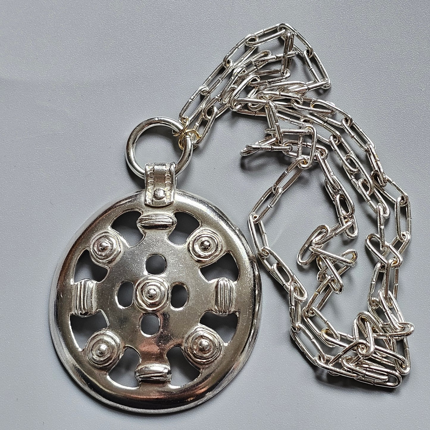 Ornate silver pendant with a circular design attached to a chain necklace.