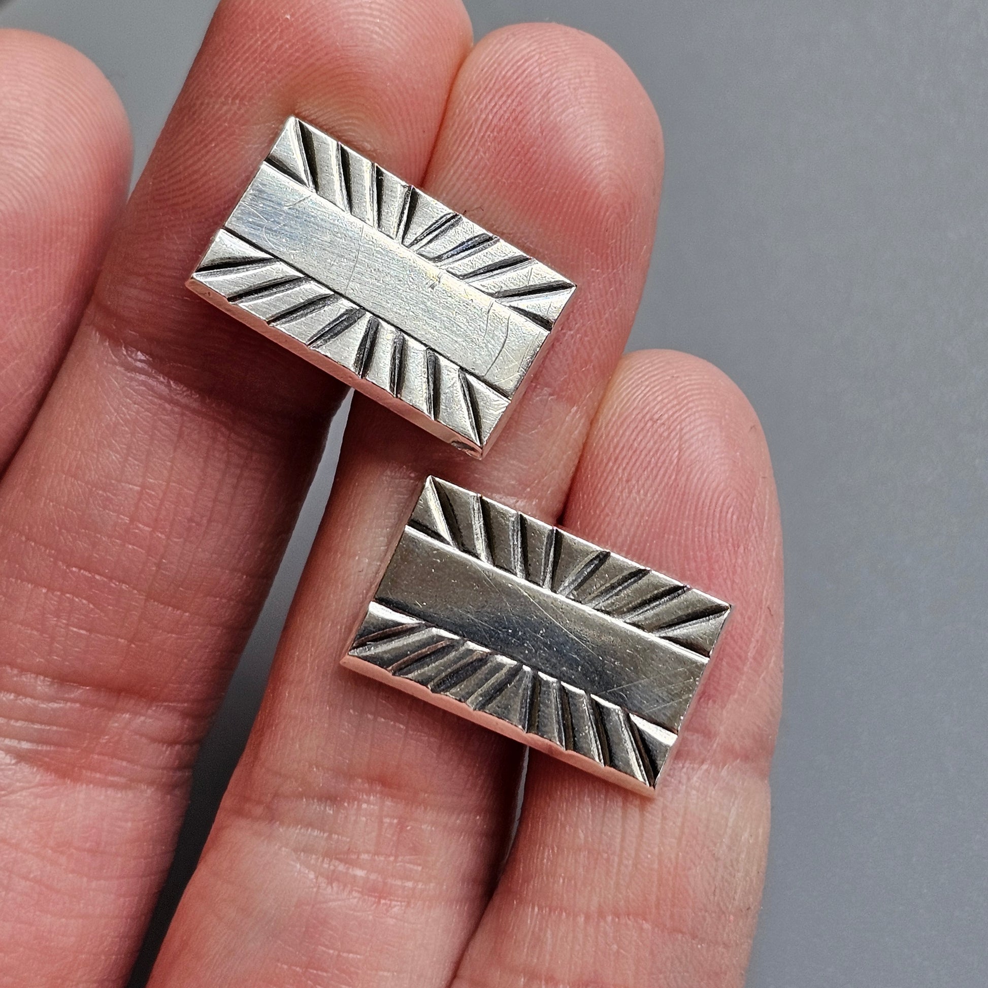 Silver rectangular cufflinks with a sunburst pattern engraved on their faces.