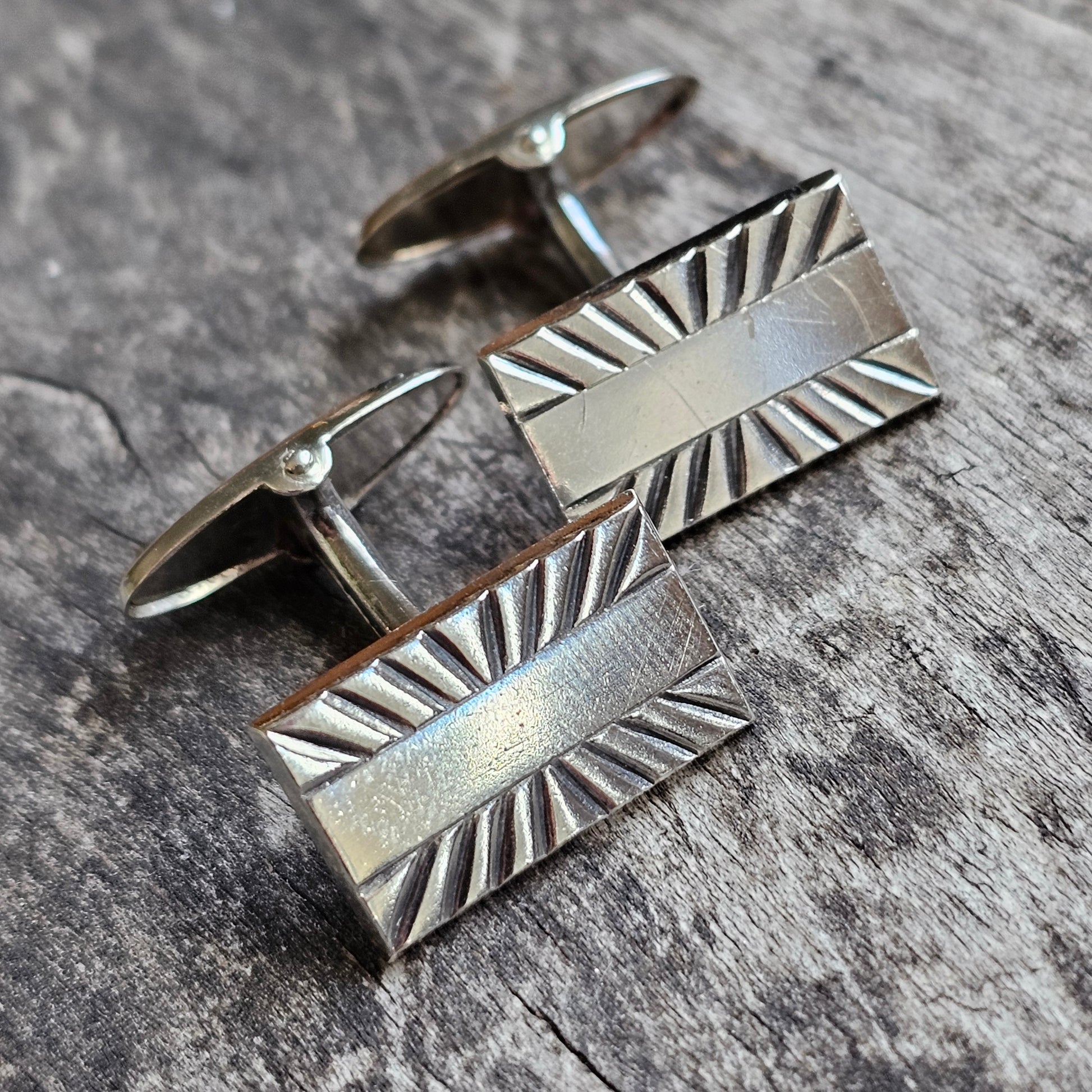 Pair of silver rectangular cufflinks with sunburst-patterned edges.