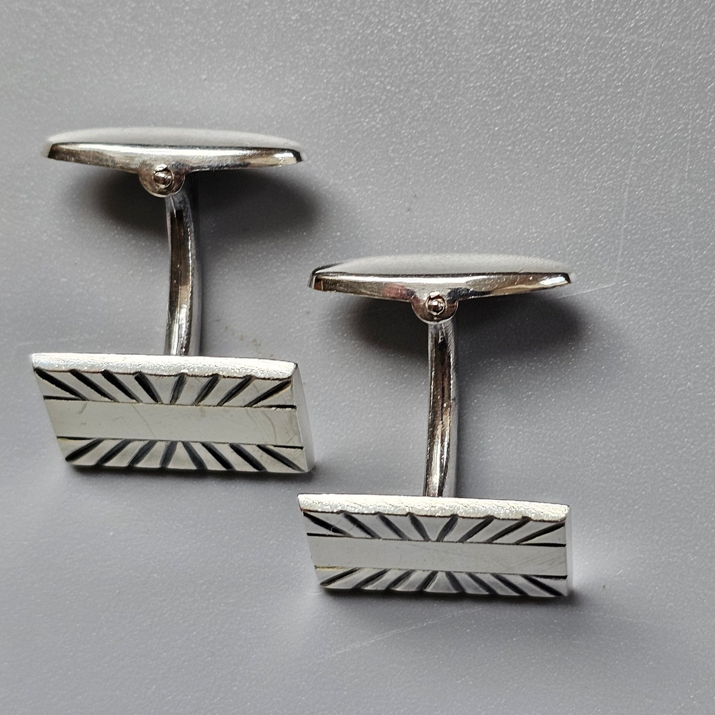 Pair of silver cufflinks with rectangular faces featuring a sunburst pattern.