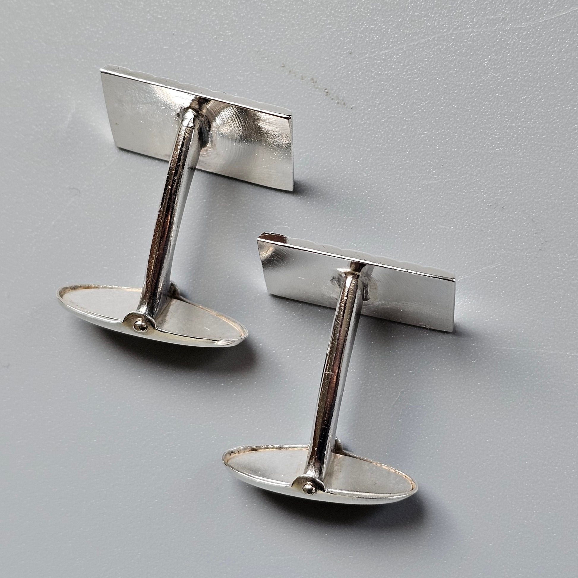 Pair of silver-colored metal cufflinks with rectangular tops and oval bases.