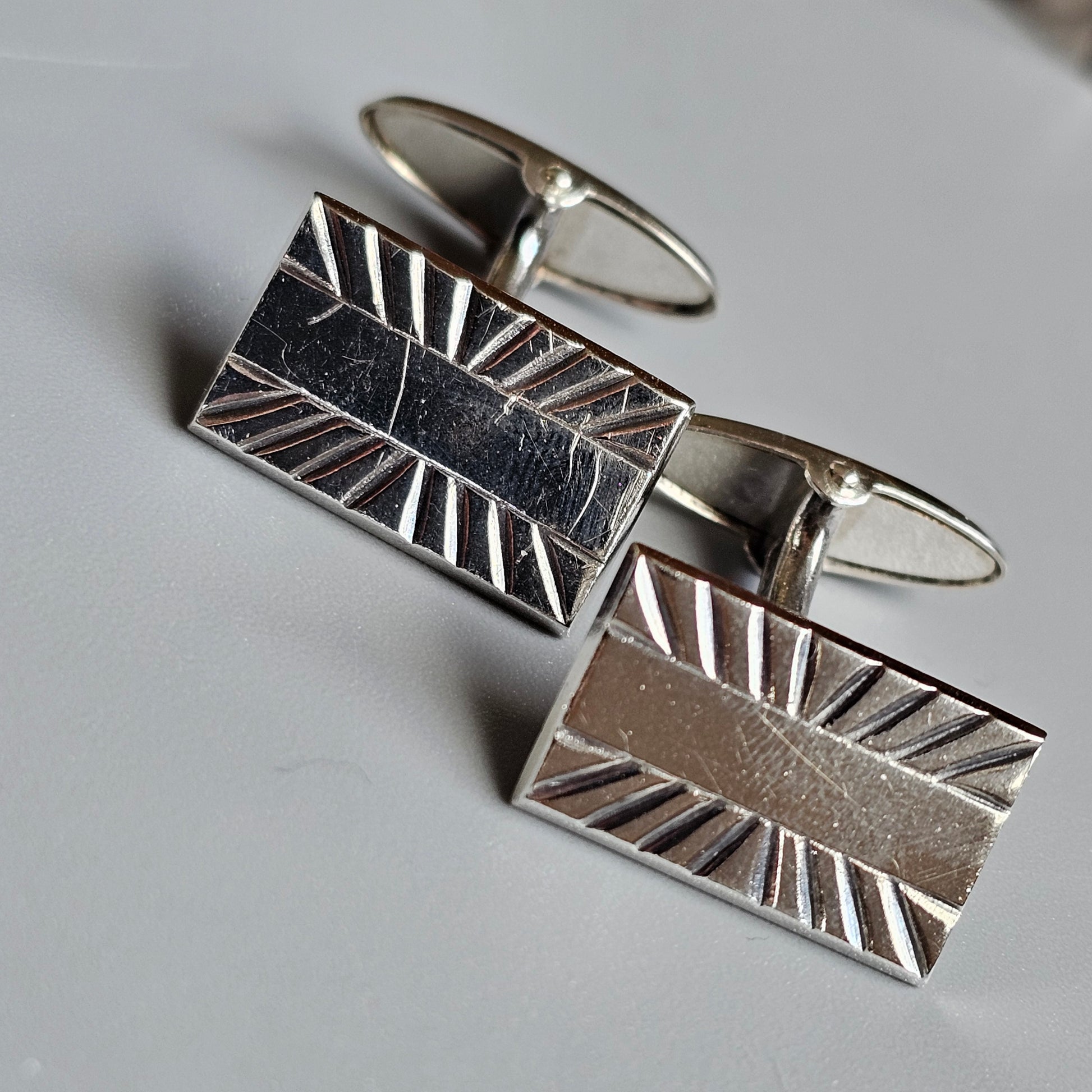 Pair of rectangular silver cufflinks with an engraved sunburst pattern.