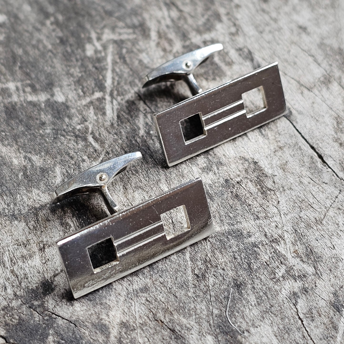 Pair of rectangular metal cufflinks with geometric cutout designs.