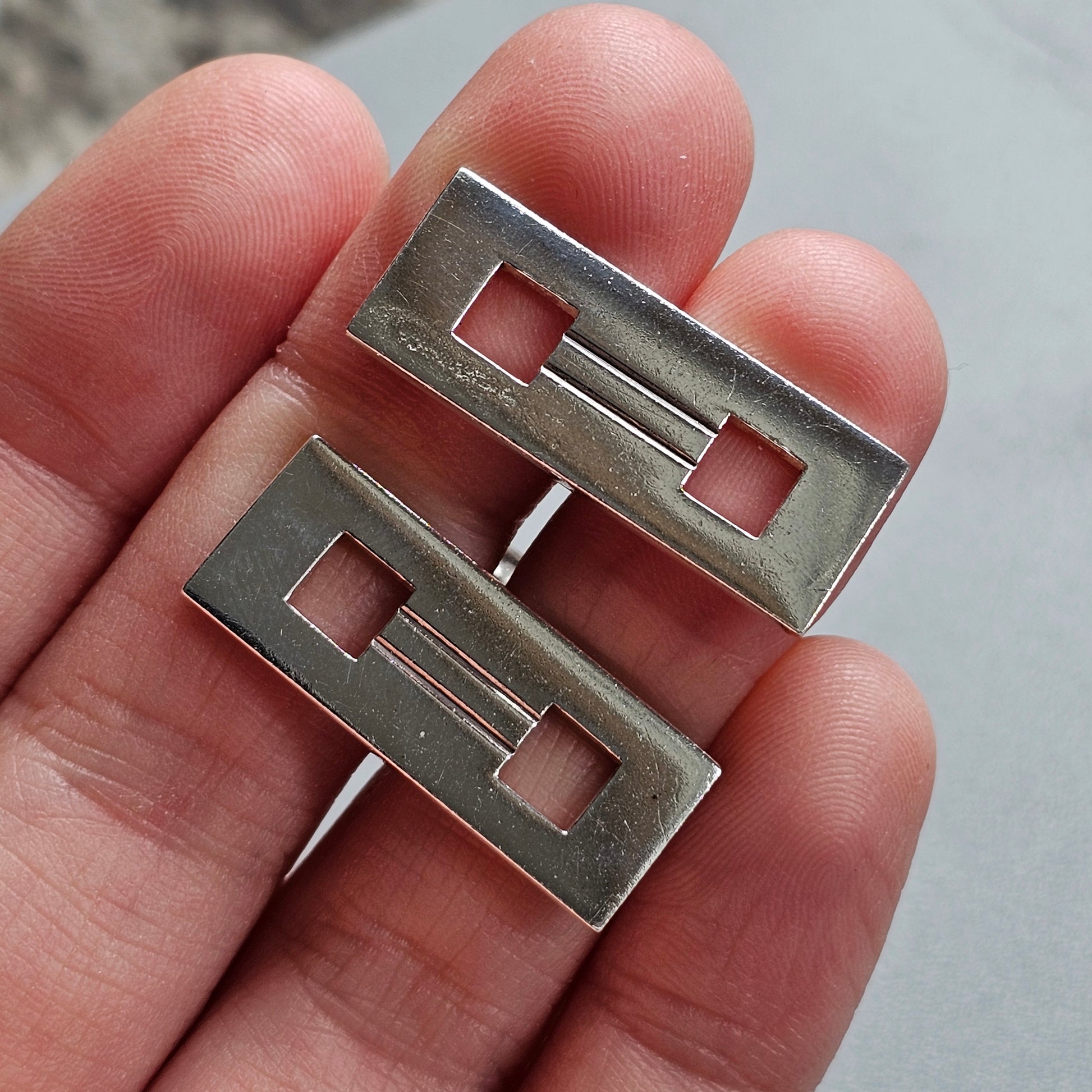 Two rectangular metal pieces with square cutouts, likely cufflinks or jewelry components.