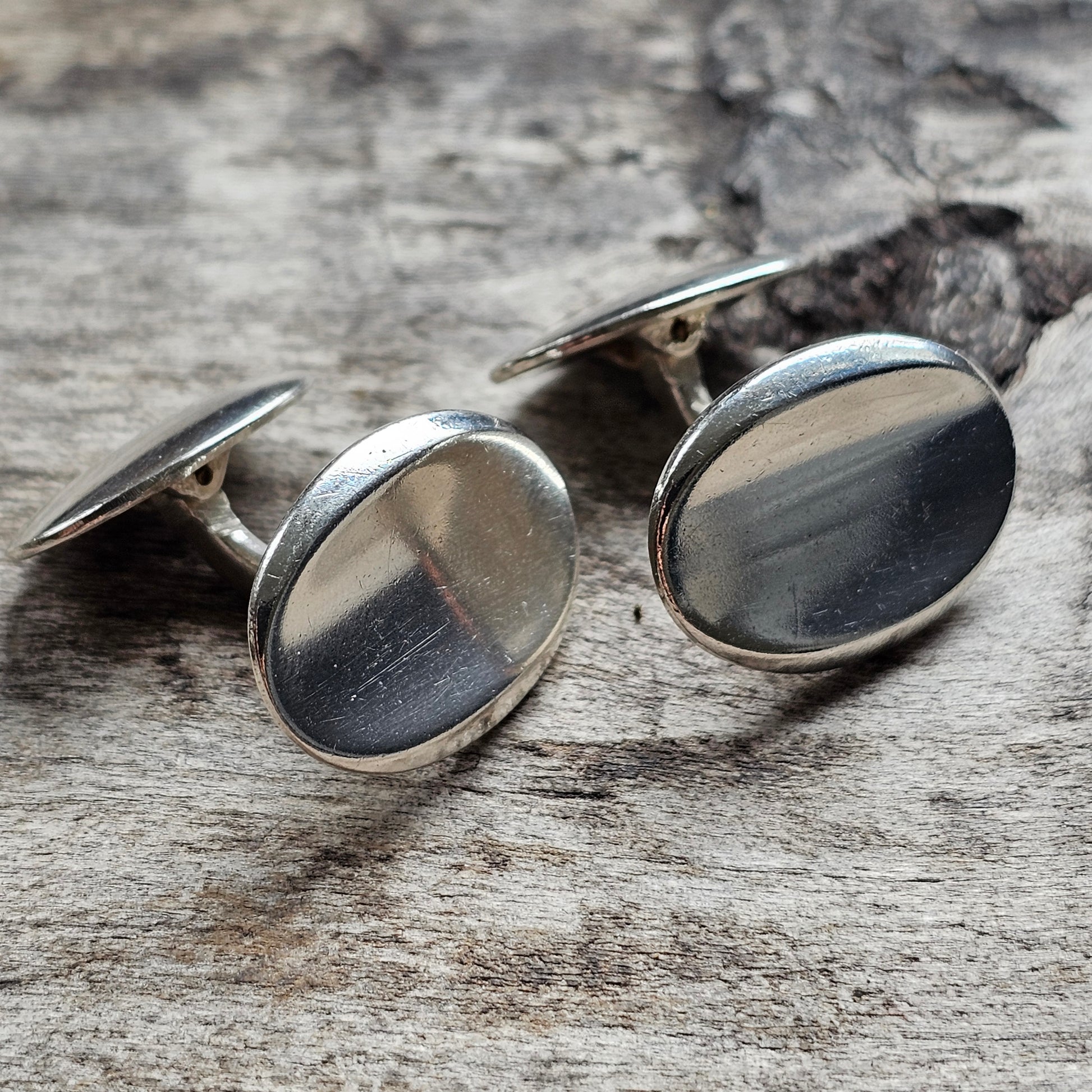 Pair of silver oval cufflinks on a textured surface.