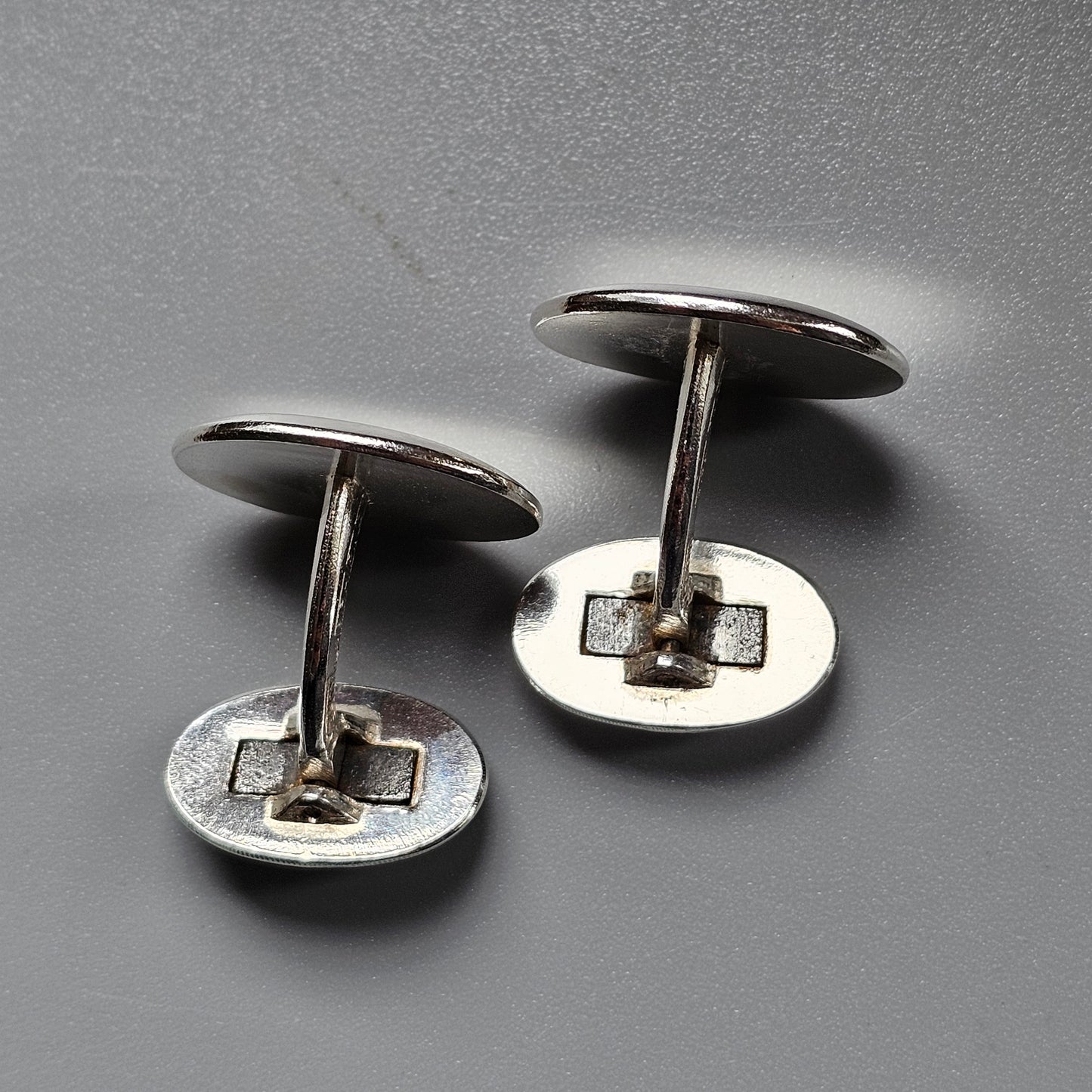 Pair of silver-colored metal cufflinks with circular faces and T-shaped backs.