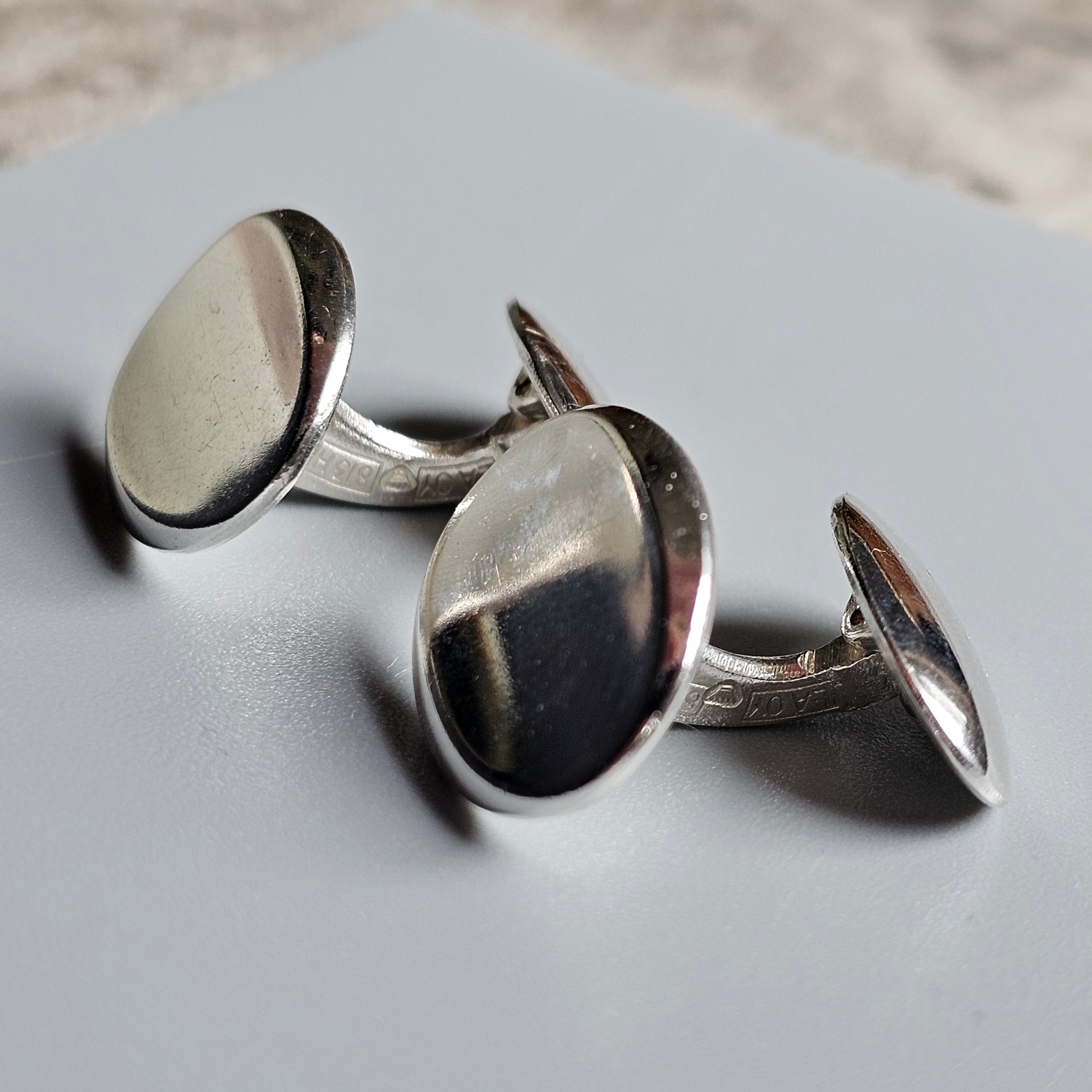 Pair of silver oval cufflinks with a polished, reflective surface.