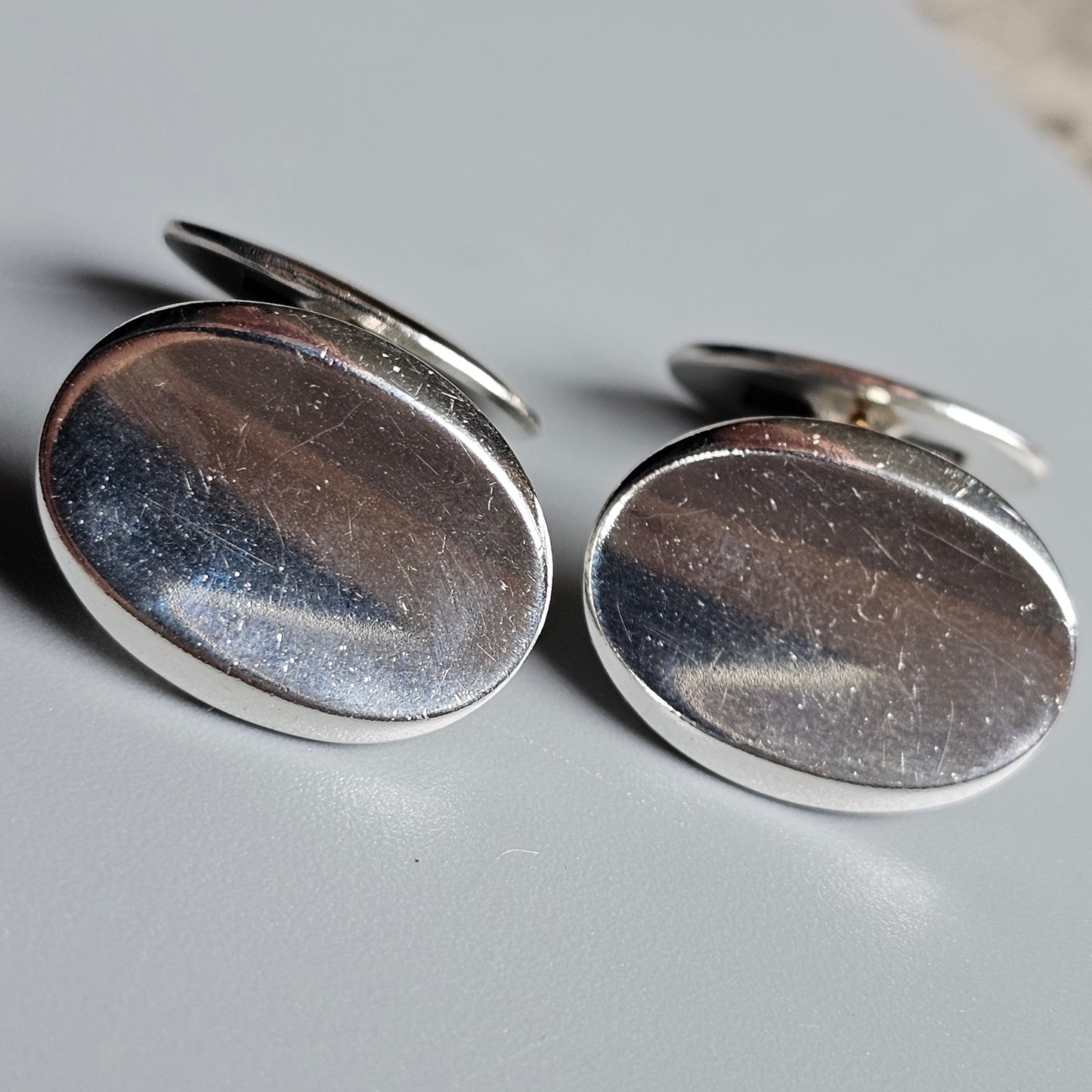 Pair of oval silver cufflinks with smooth, reflective surfaces.