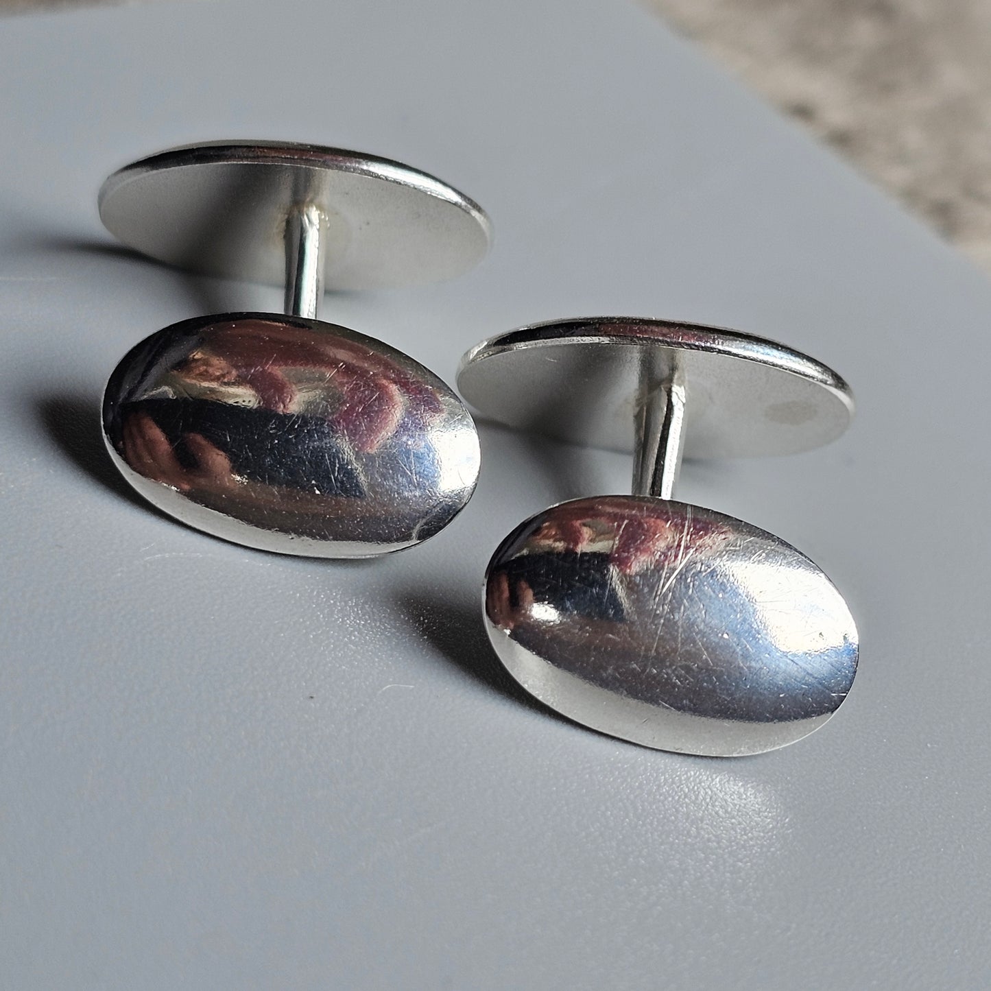 Pair of oval silver cufflinks with reflective surfaces.