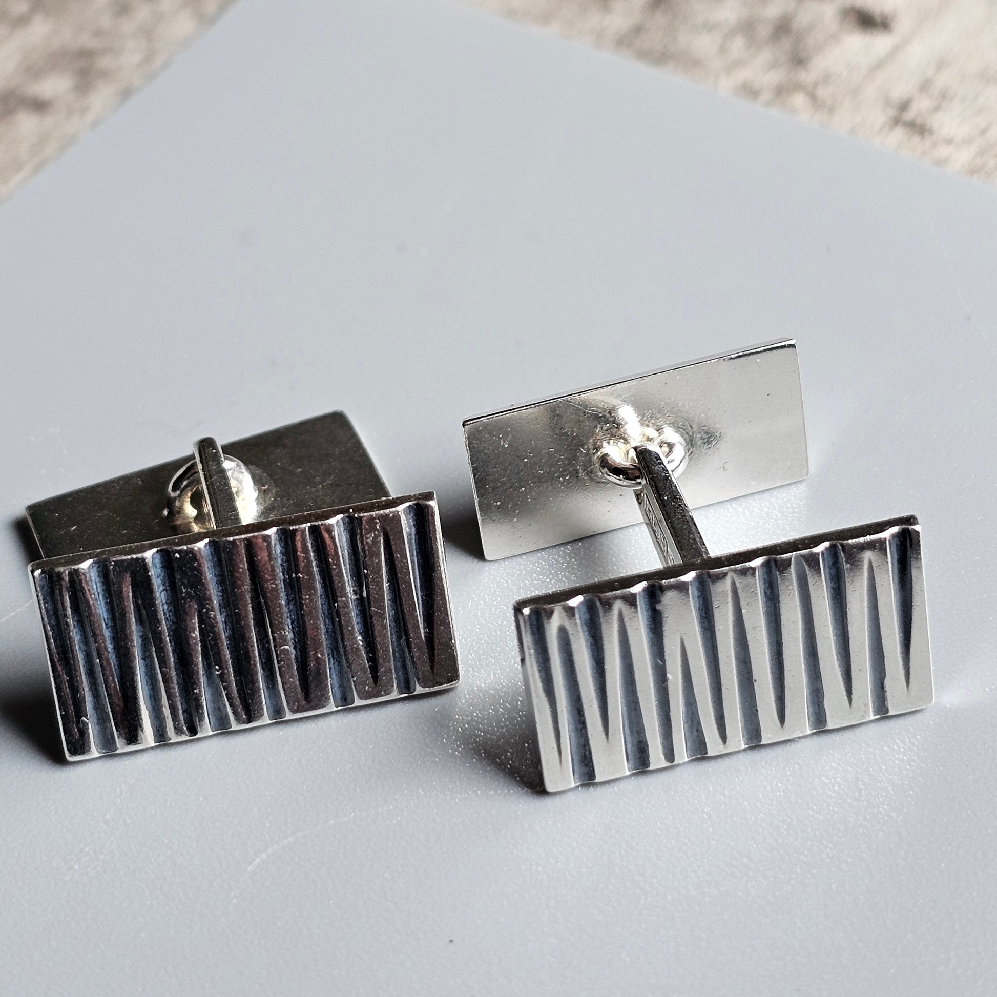 Pair of rectangular silver cufflinks with vertical ridged patterns.