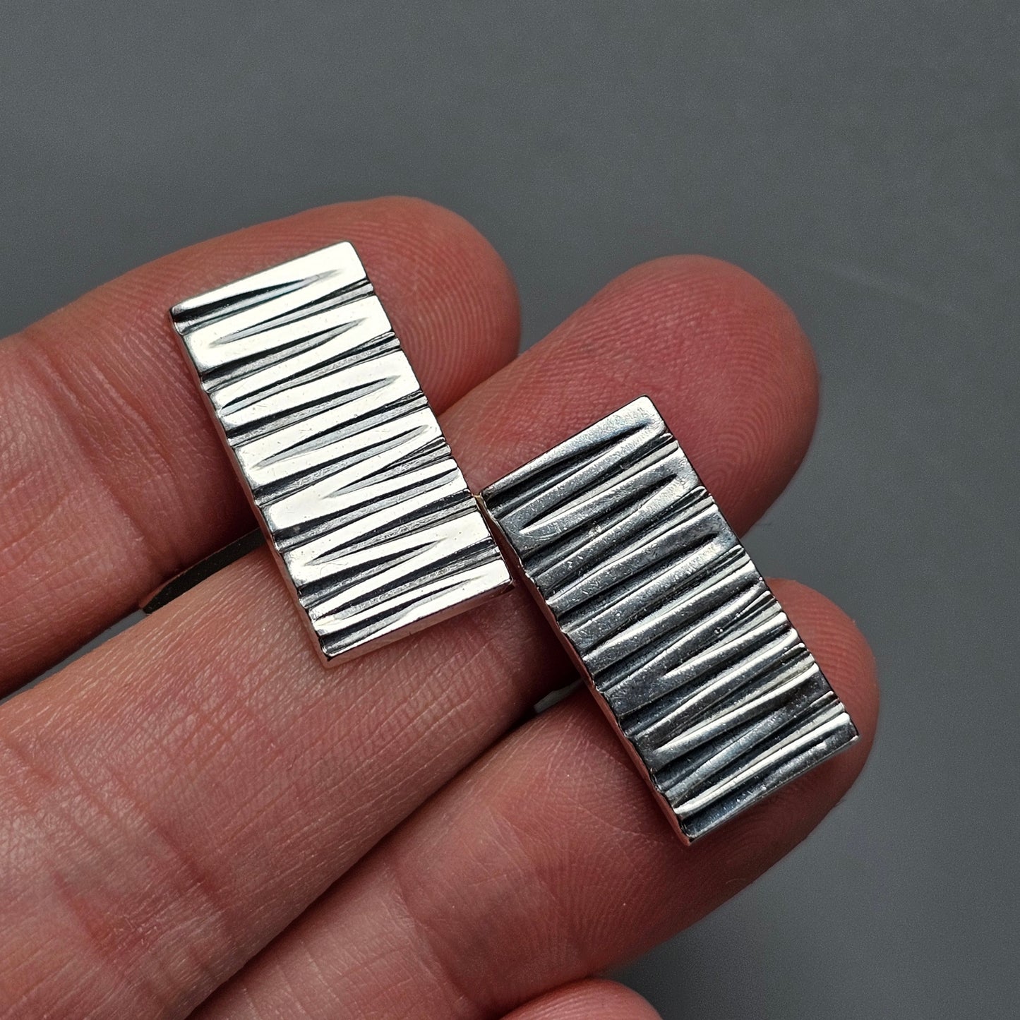 Two rectangular metal objects with parallel ridges held between fingertips.