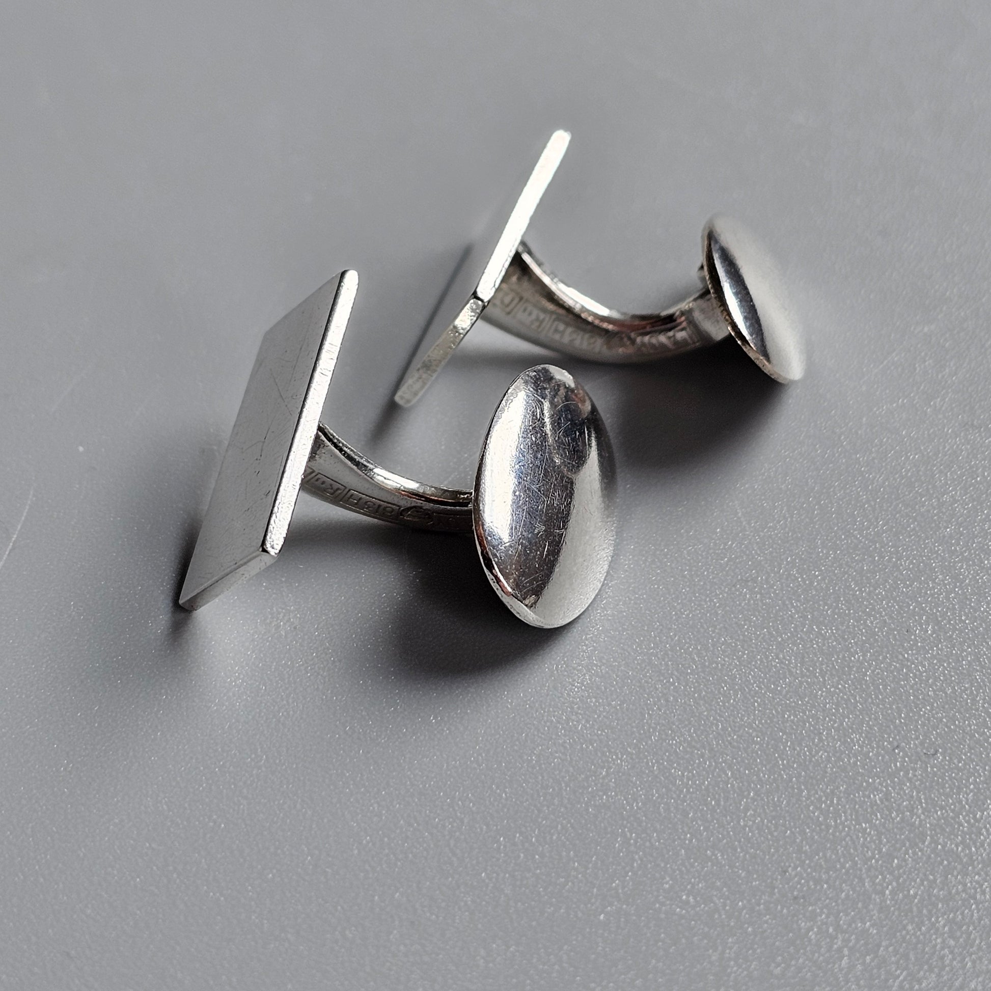 Pair of silver cufflinks with rectangular and oval shapes.