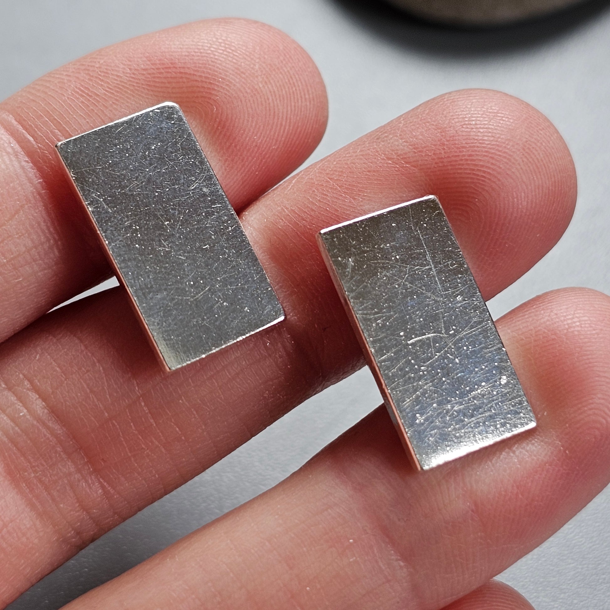 Two rectangular silver metal bars held between fingertips.