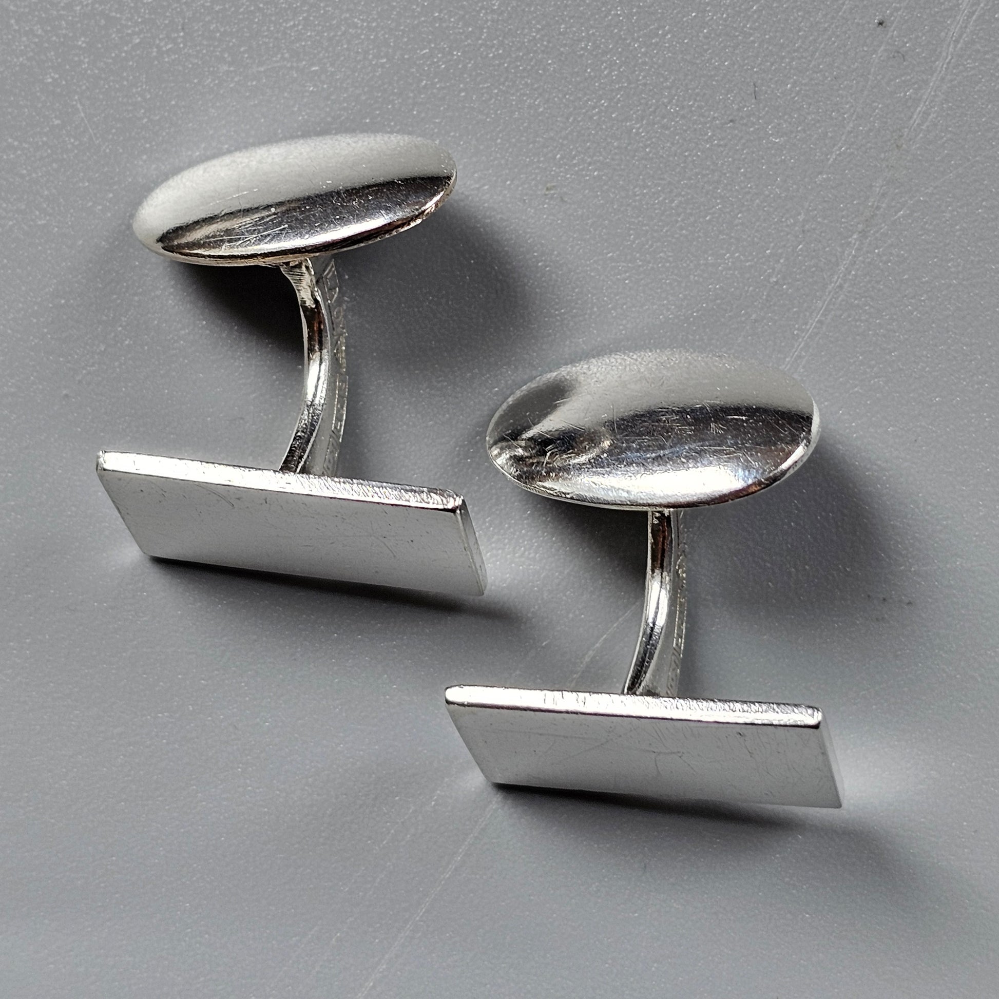 Pair of silver cufflinks with rectangular faces and curved stems.