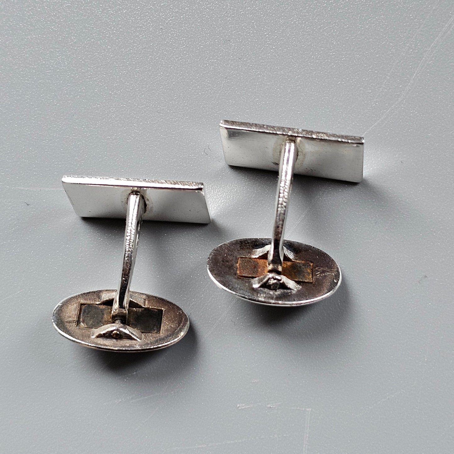 Pair of silver-colored metal cufflinks with rectangular tops and circular bases.