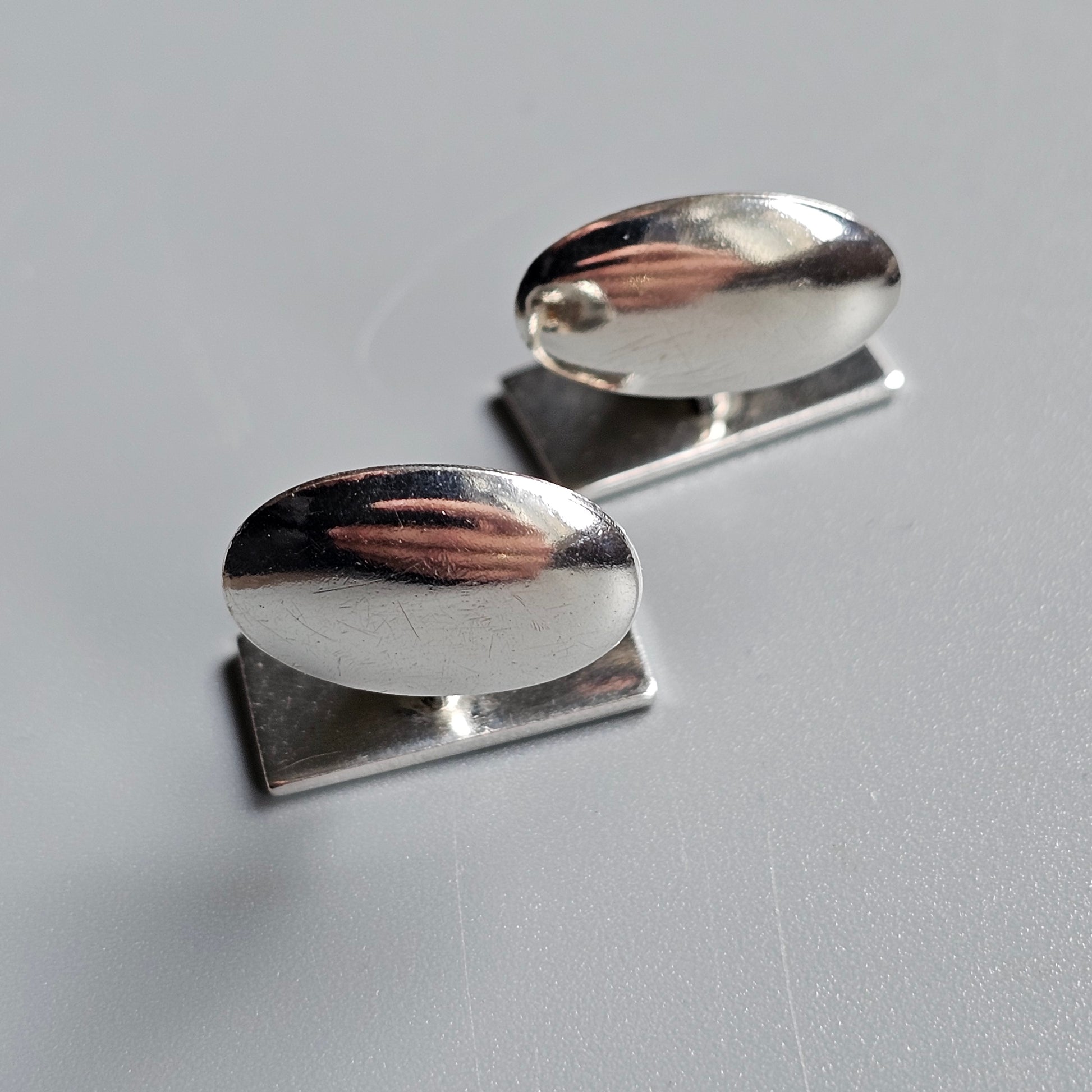 Pair of oval silver cufflinks with smooth, reflective surfaces.