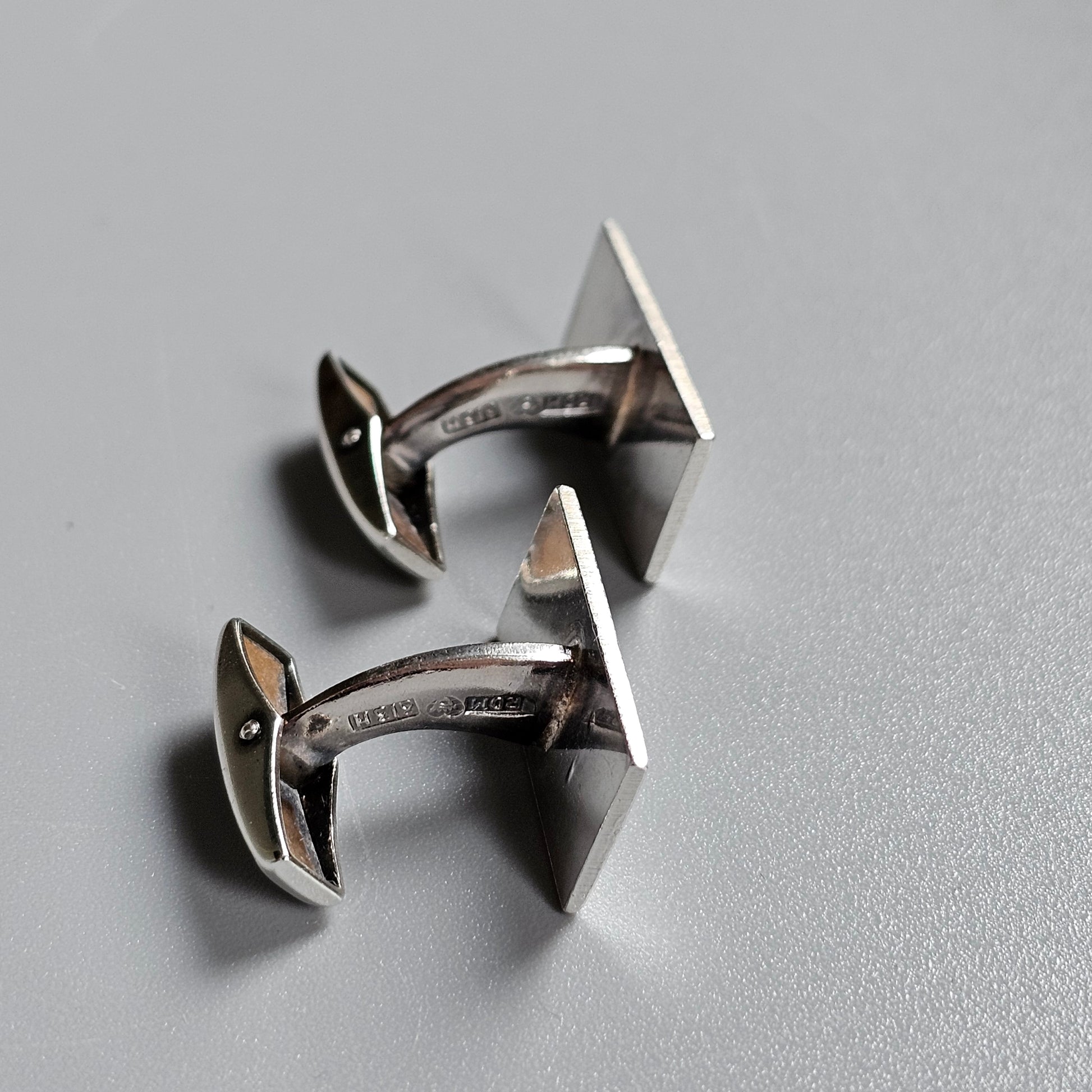 Pair of silver-colored cufflinks shaped like angular letters or symbols.