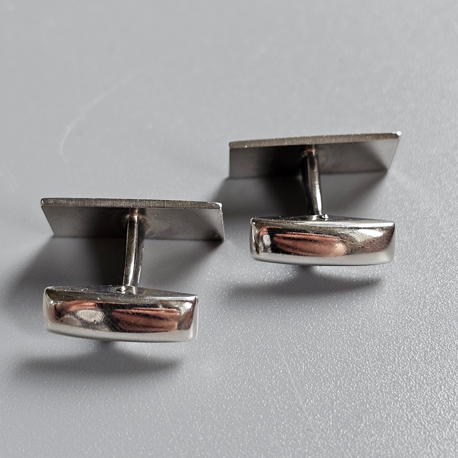 Pair of silver cufflinks with rectangular faces and curved edges.