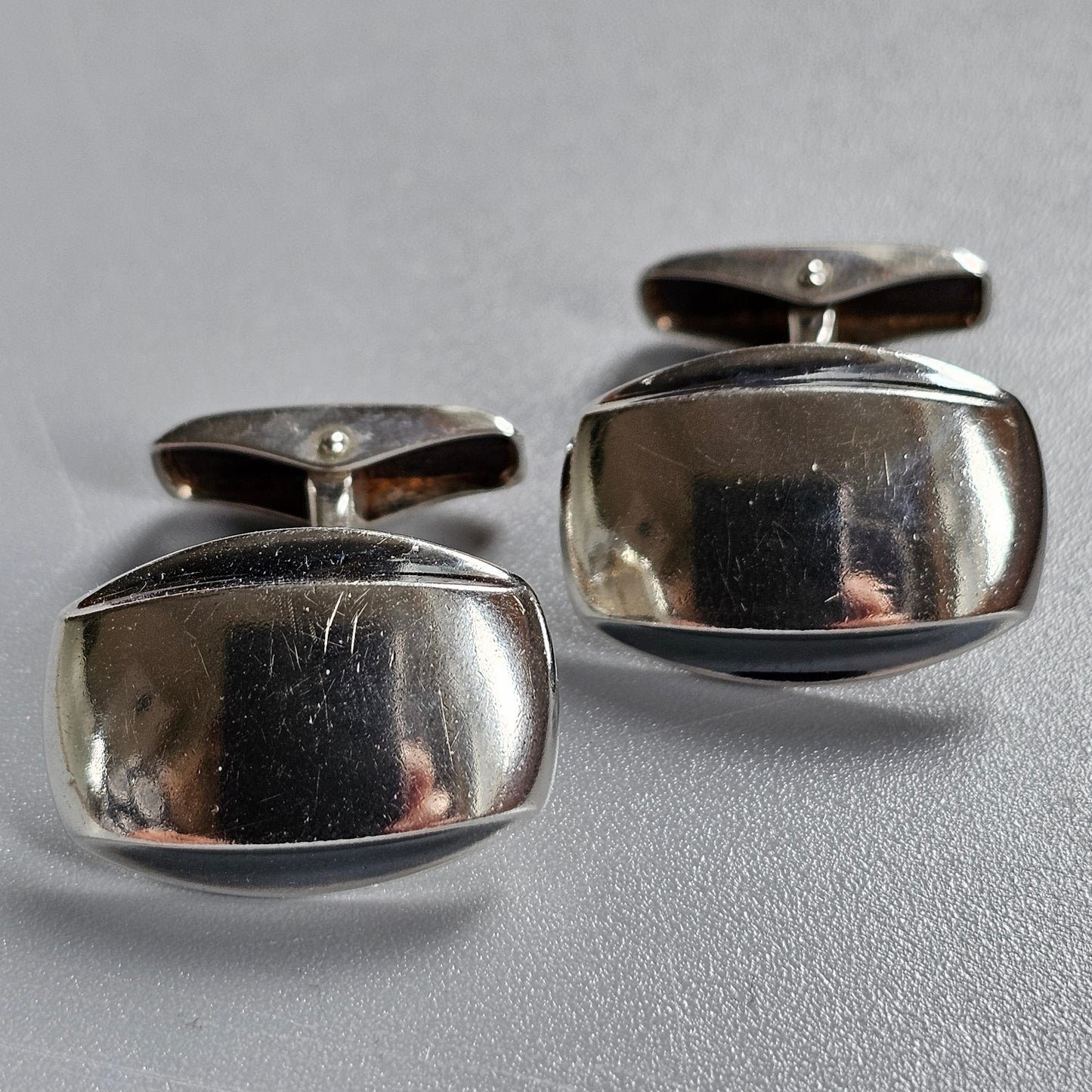 Pair of shiny silver cufflinks with smooth, rounded rectangular shapes.