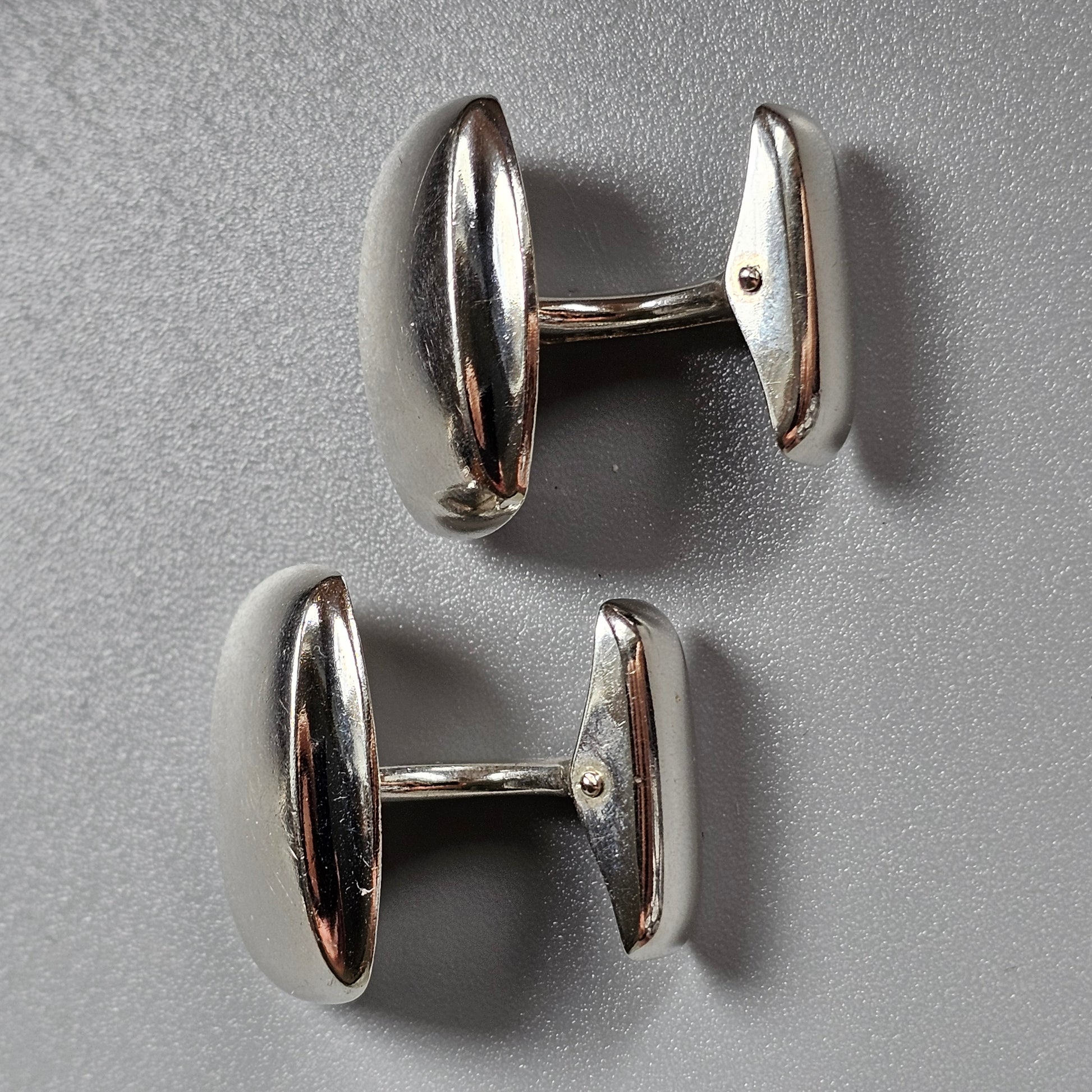 Pair of silver oval cufflinks with smooth, reflective surfaces.