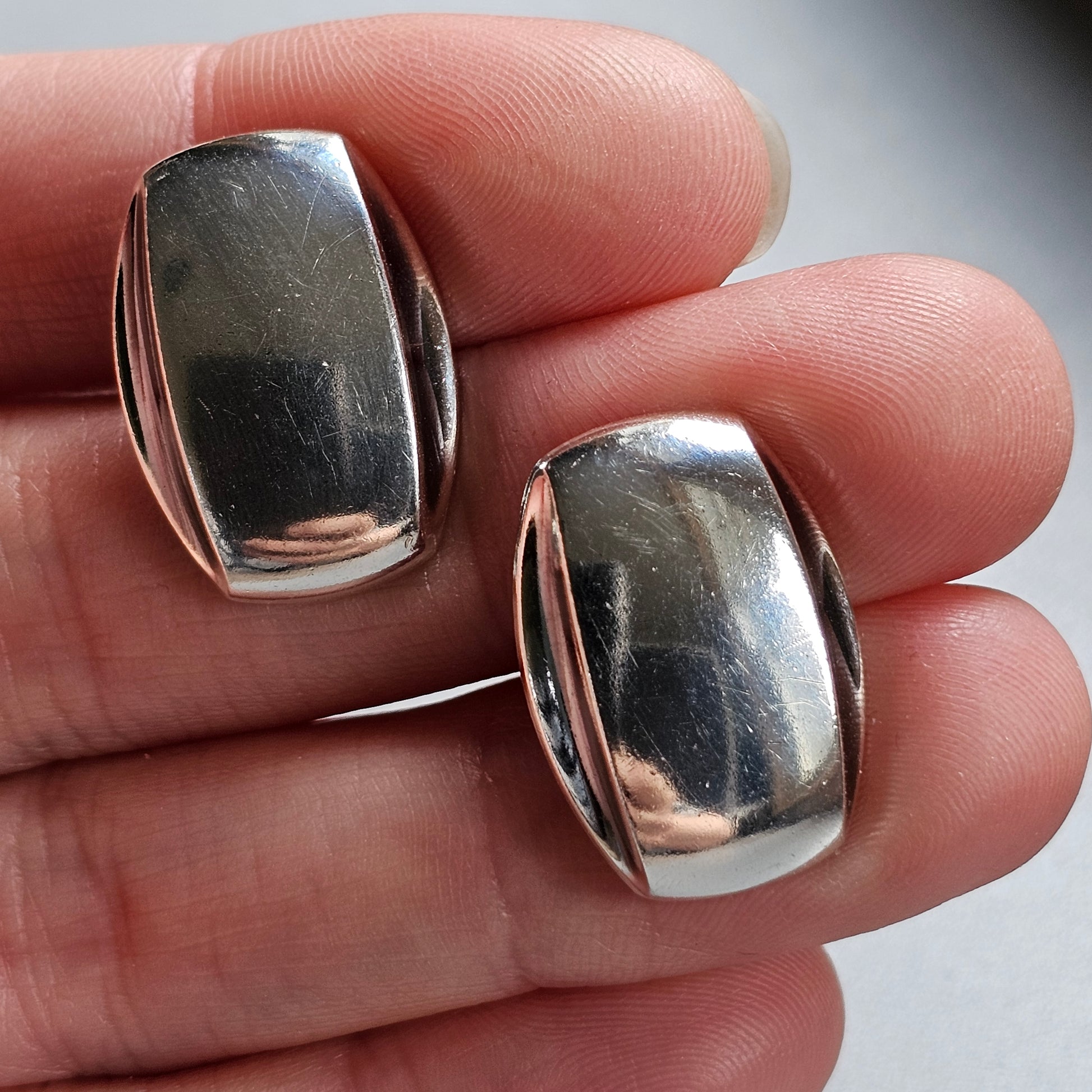 Pair of shiny, oval-shaped silver earrings held between fingers.