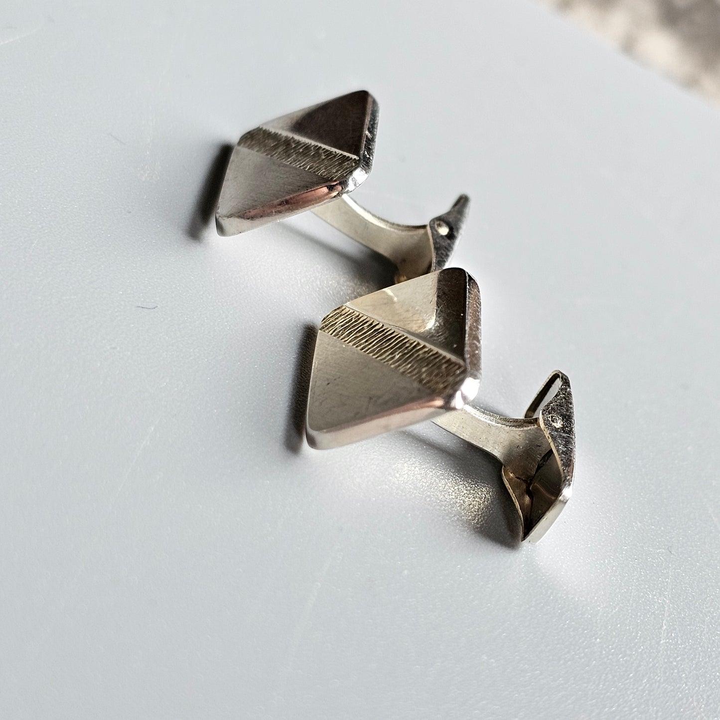 Pair of silver triangular cufflinks with textured edges.