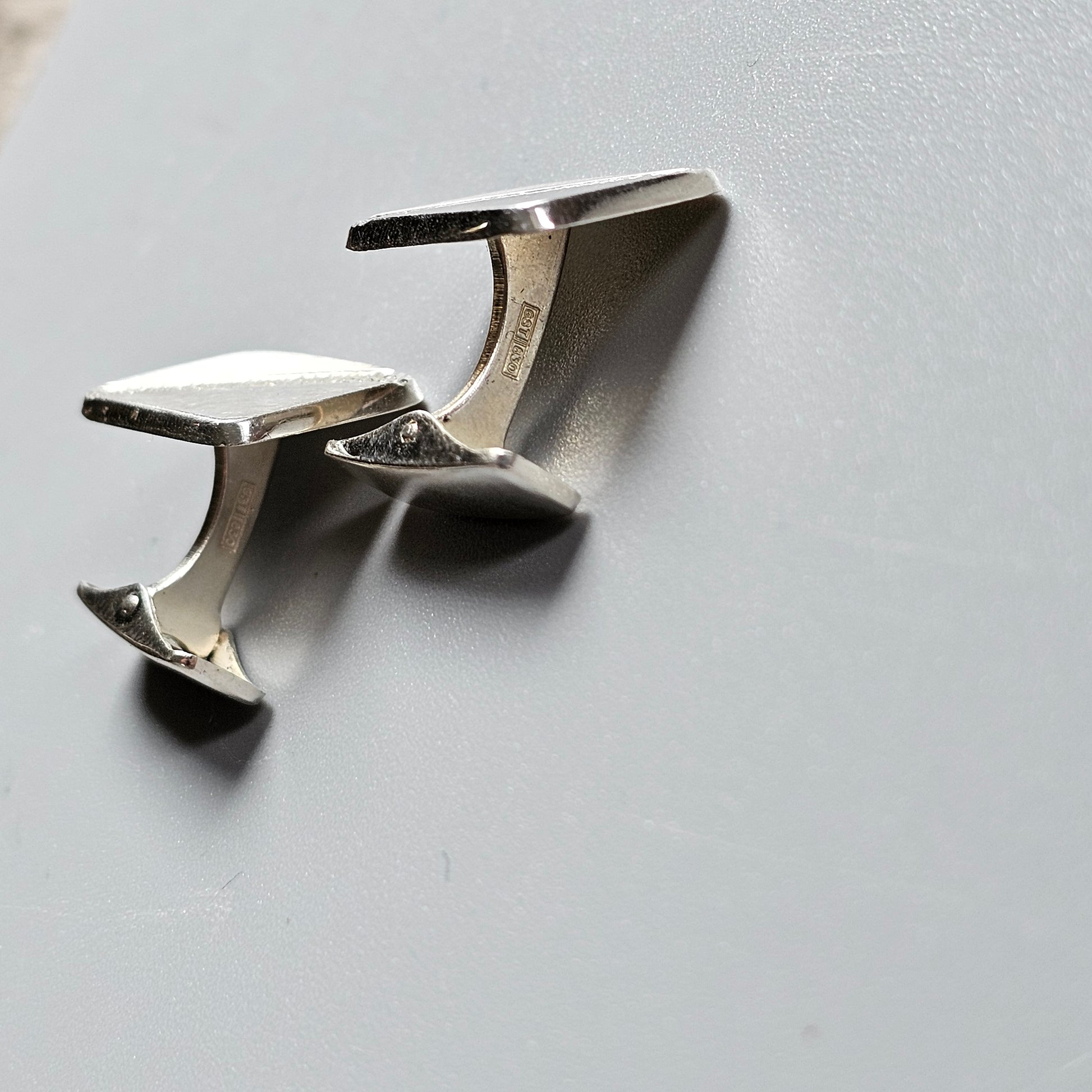 Silver cufflink with a sleek, modern design featuring two rectangular surfaces connected by a curved bar.