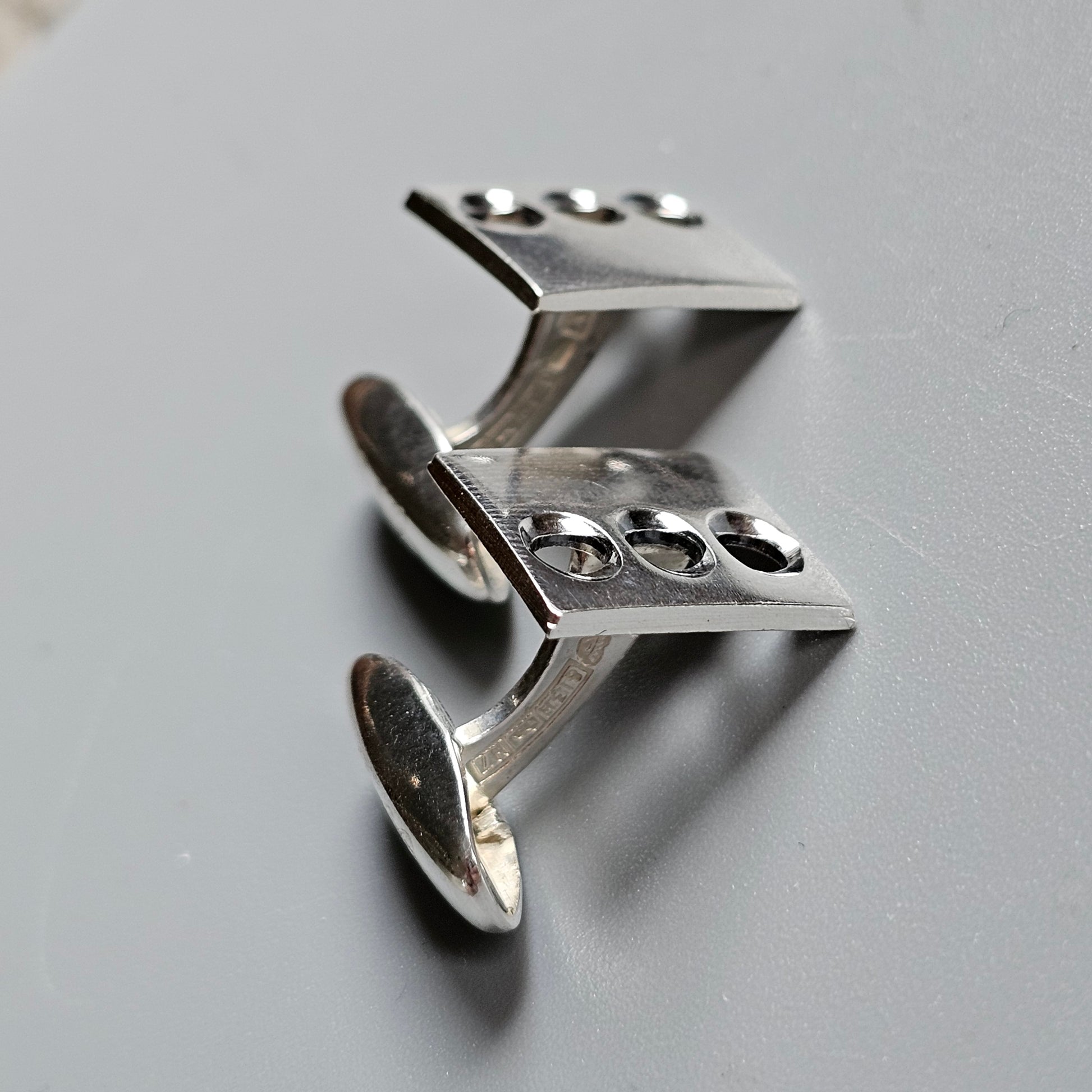 Silver cufflinks with a unique angular design featuring circular cutouts.