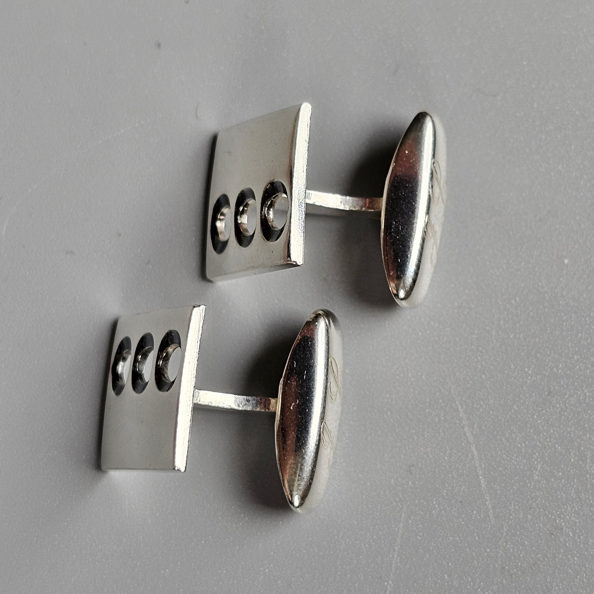 Pair of silver cufflinks with three circular cutouts on each rectangular face.