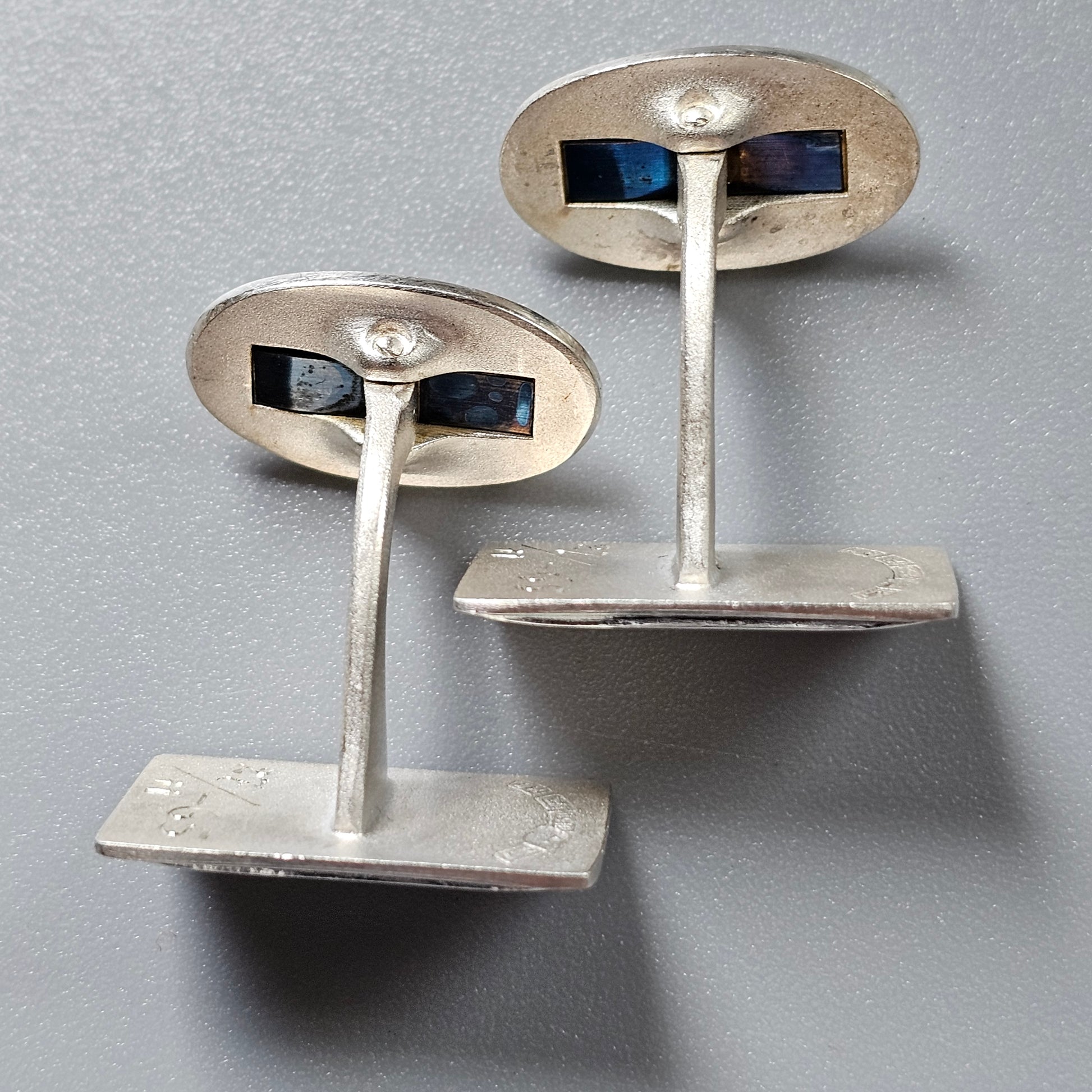 Pair of silver cufflinks with oval faces and blue inlaid accents.