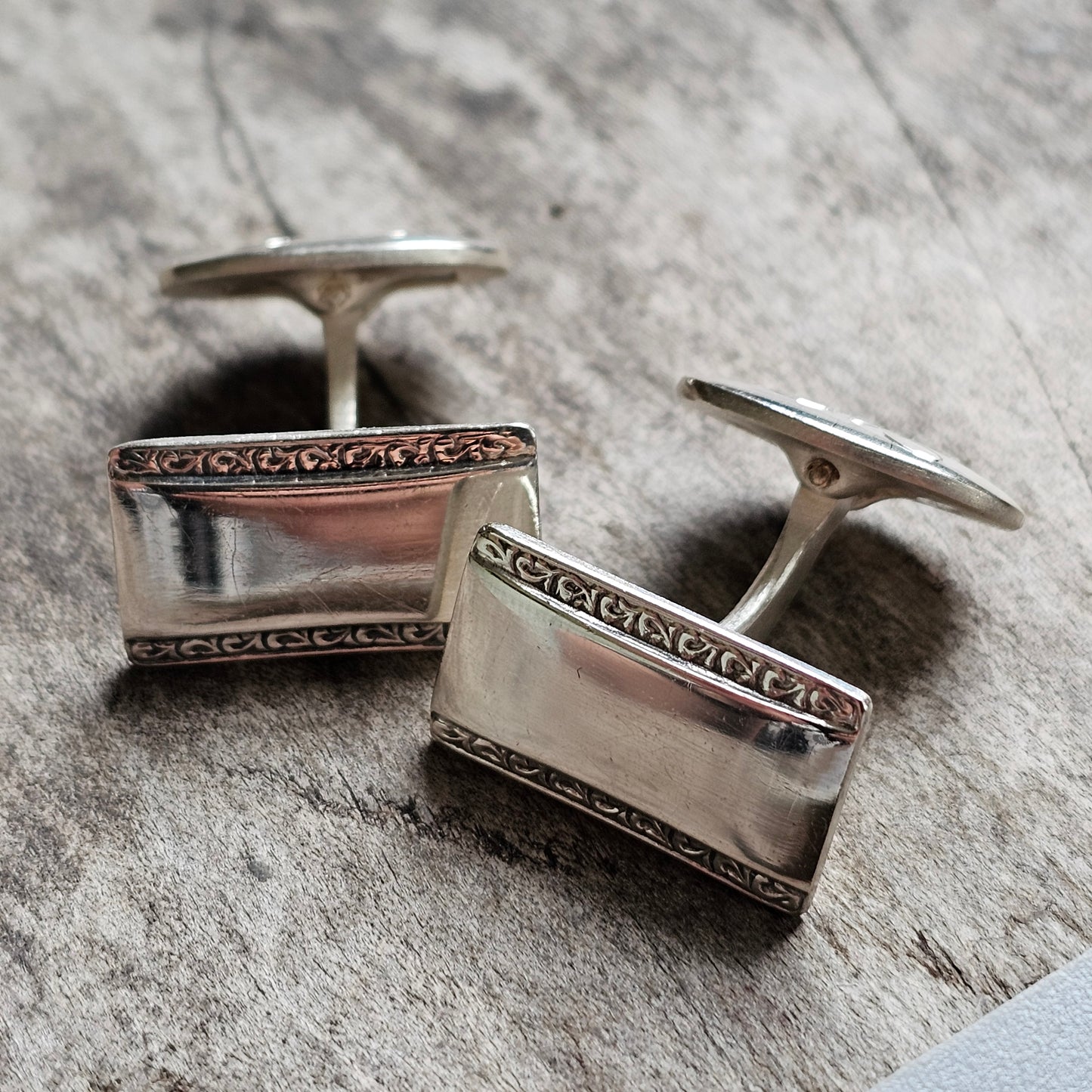 Pair of silver rectangular cufflinks with decorative borders.