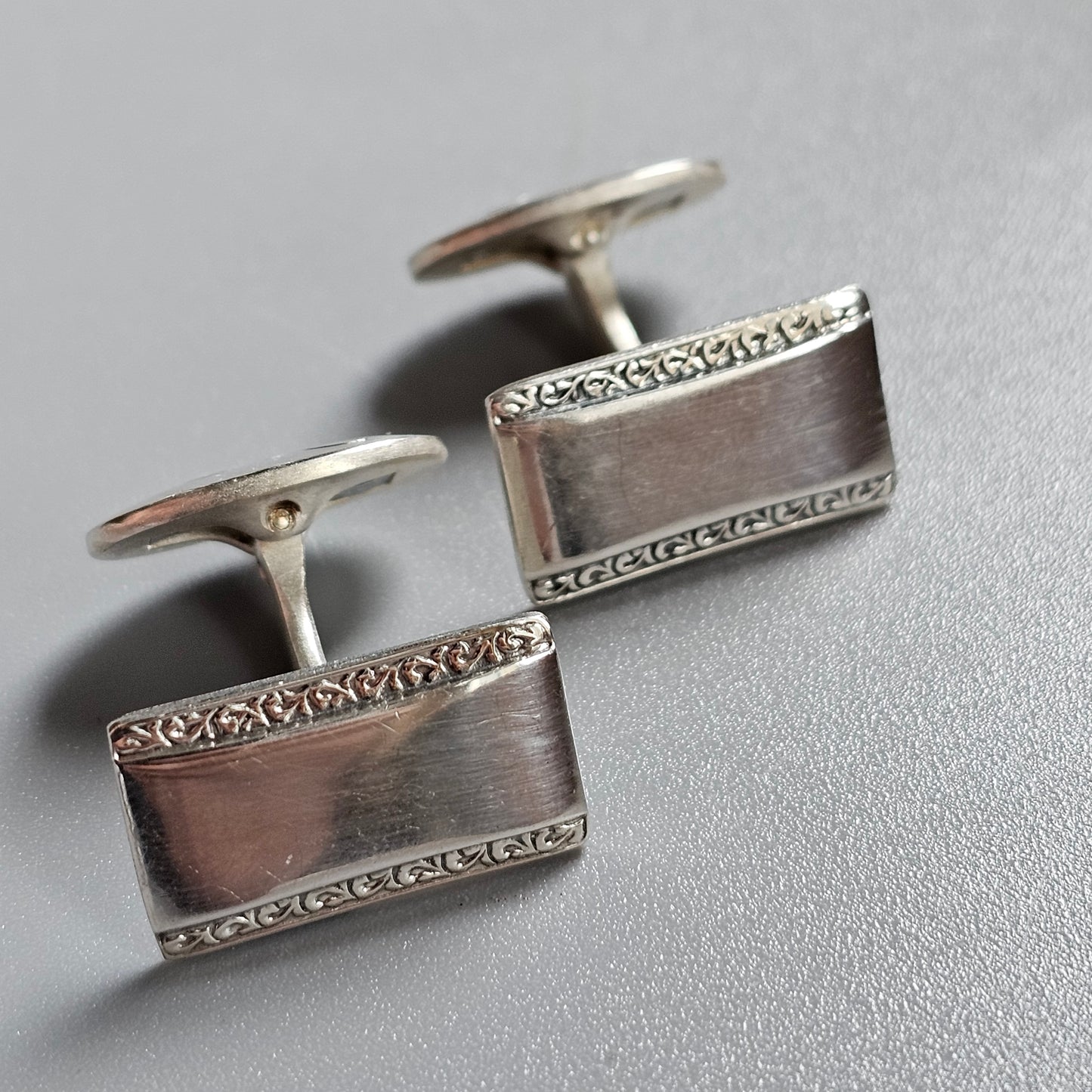 Pair of rectangular silver cufflinks with decorative borders.