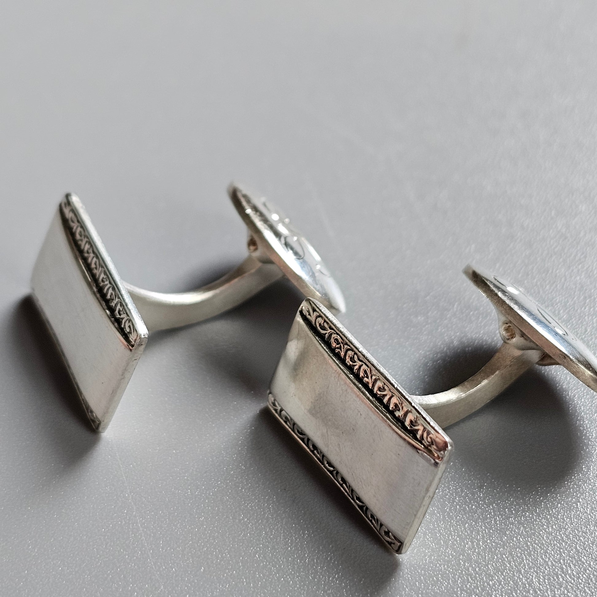 Pair of silver square cufflinks with decorative edges.