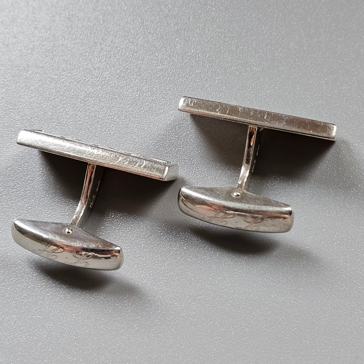 Pair of silver-colored metal cufflinks with rectangular tops and curved bases.