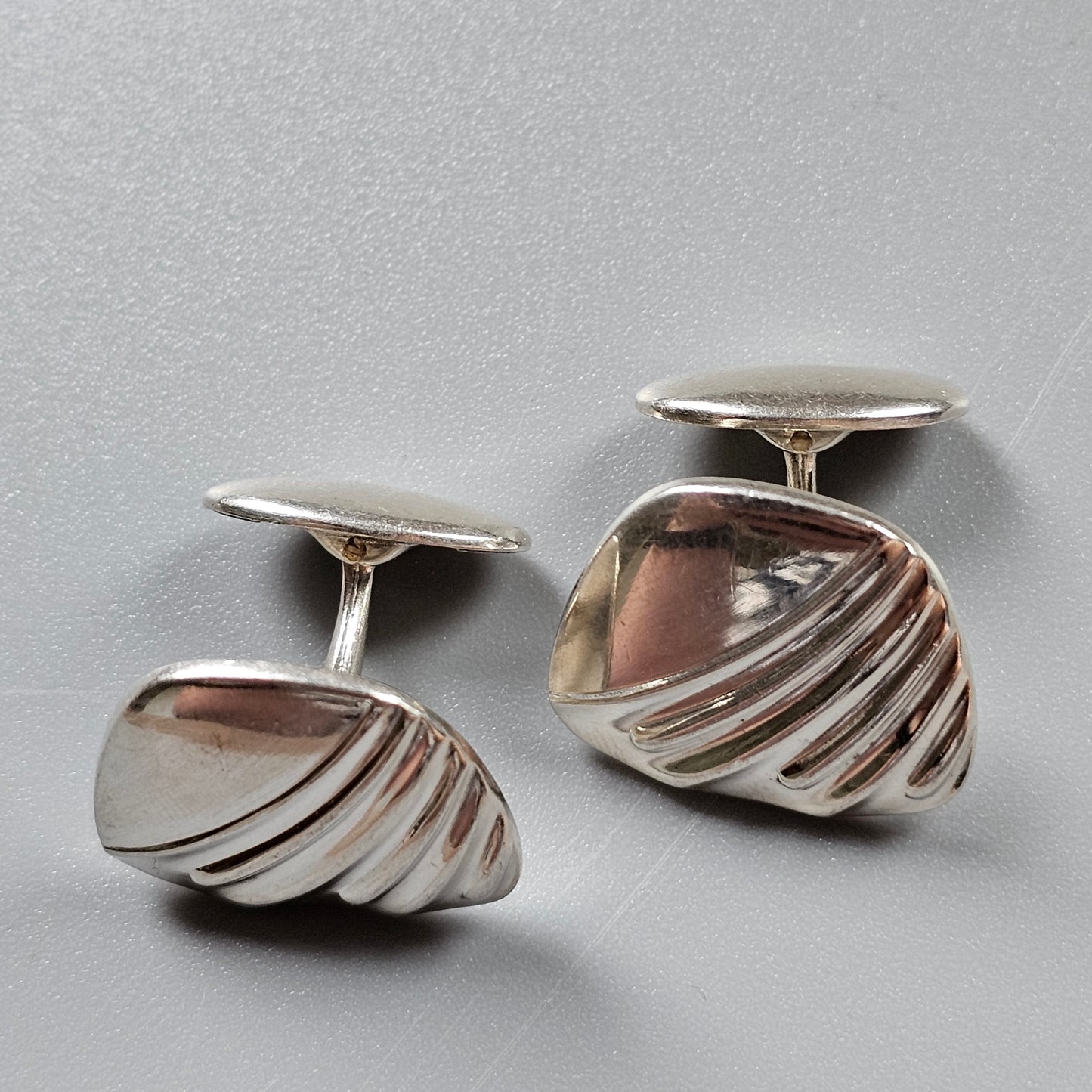 Pair of silver cufflinks with a curved, ridged design.