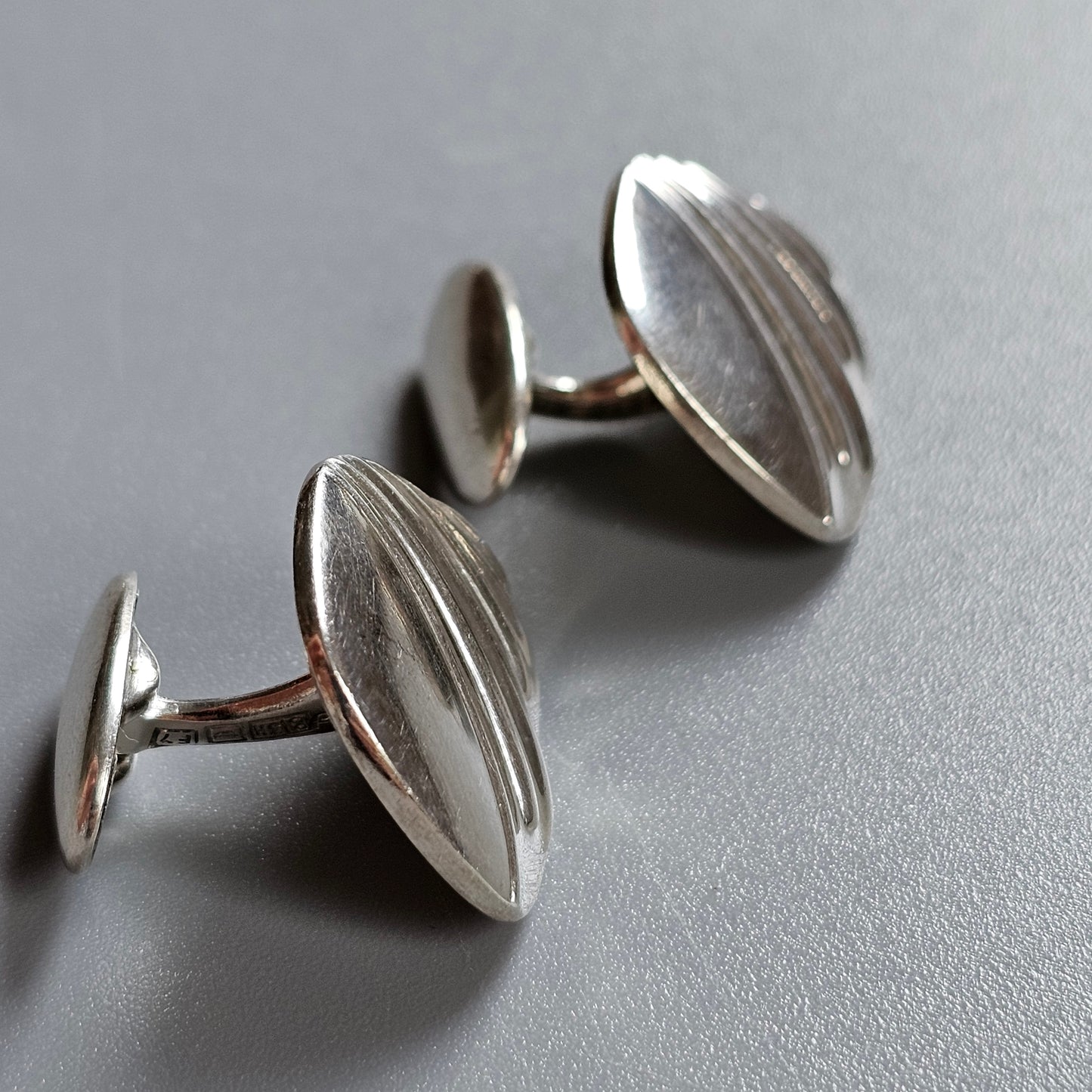 Pair of silver oval cufflinks with subtle ridged designs.