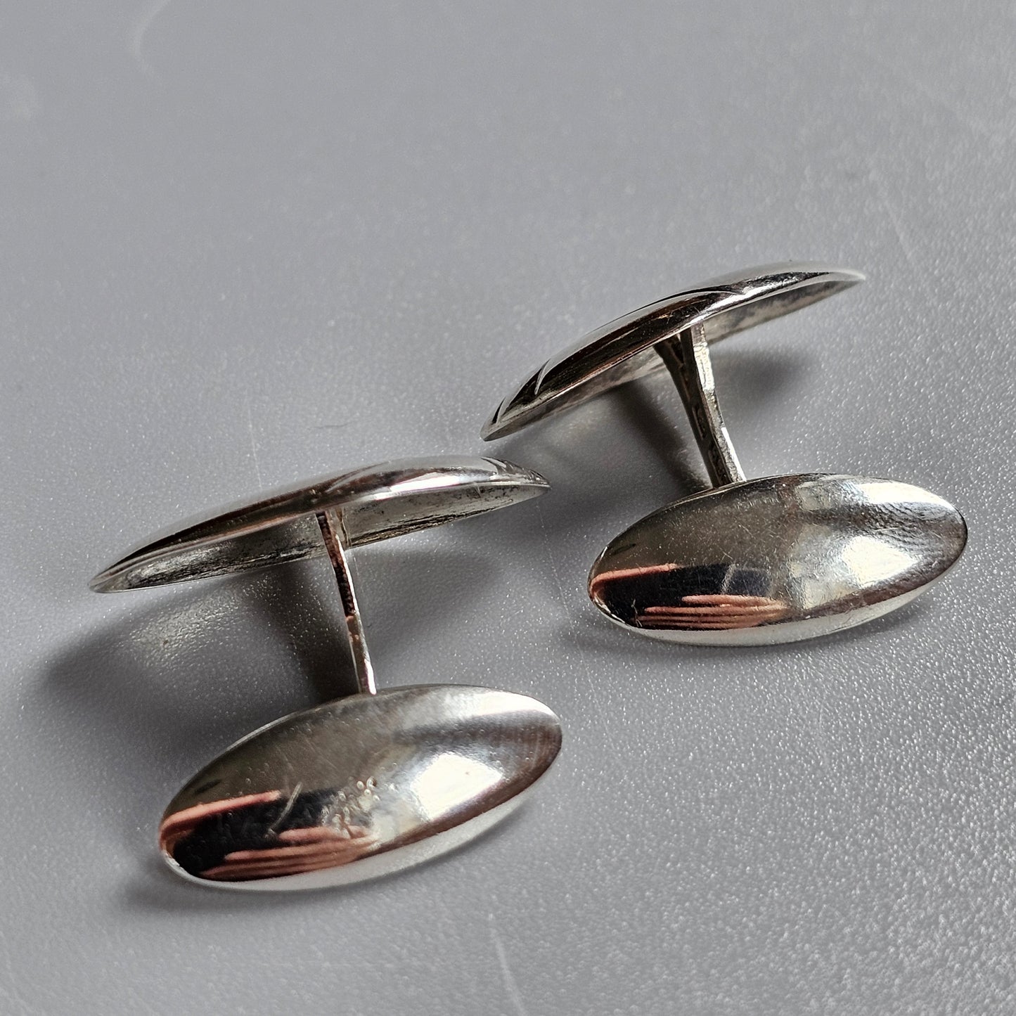 Pair of oval silver cufflinks with smooth, reflective surfaces.