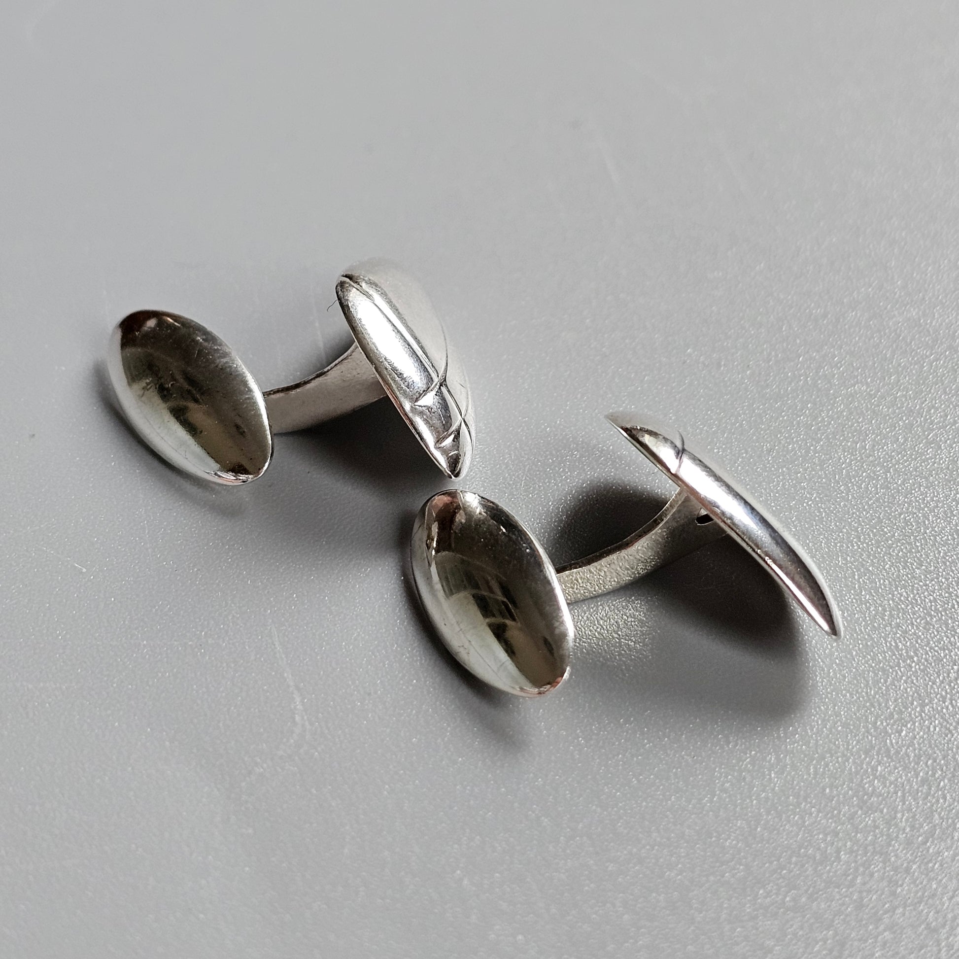 Pair of silver oval cufflinks with smooth, reflective surfaces.