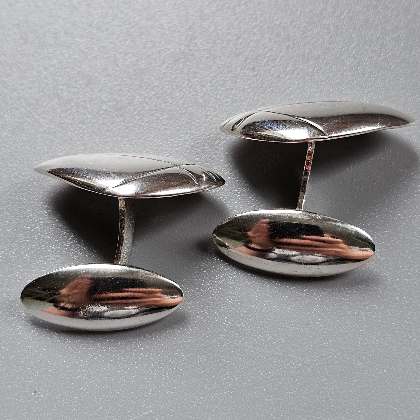 Pair of silver oval cufflinks with reflective surfaces.