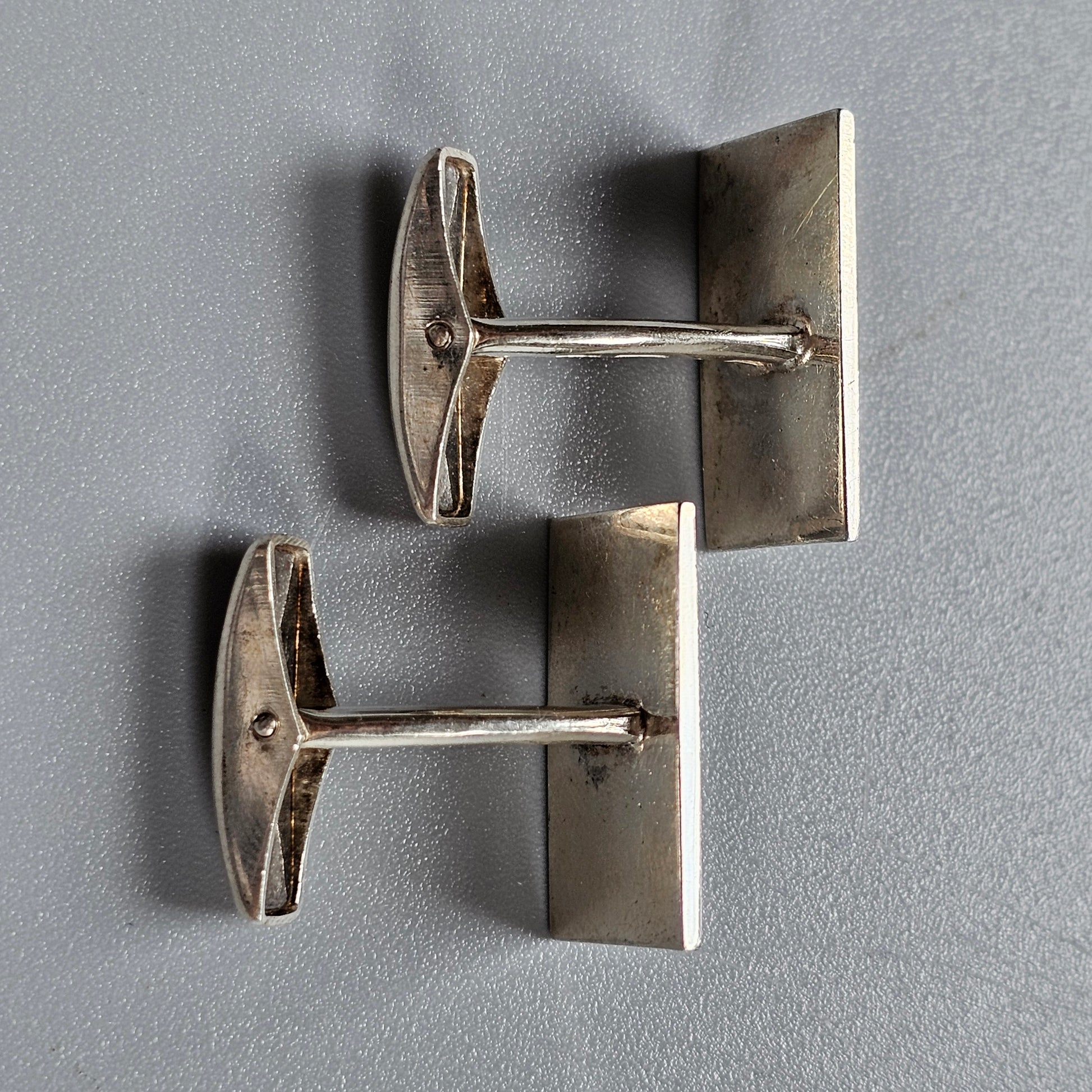 Pair of silver-colored metal cufflinks with rectangular faces and T-shaped bars.