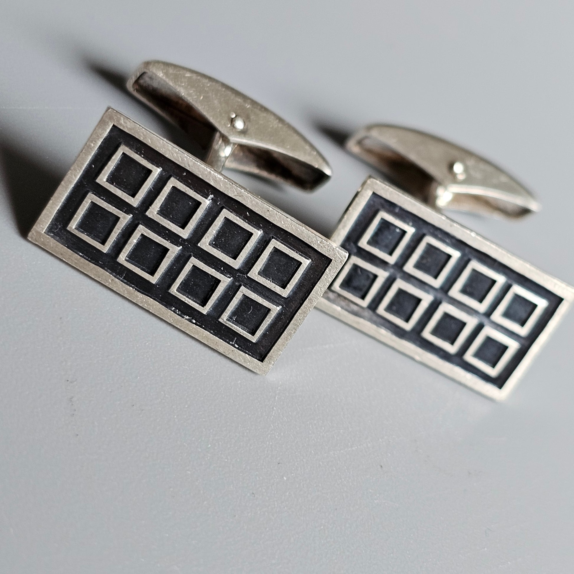 Pair of rectangular silver cufflinks with a black geometric pattern.