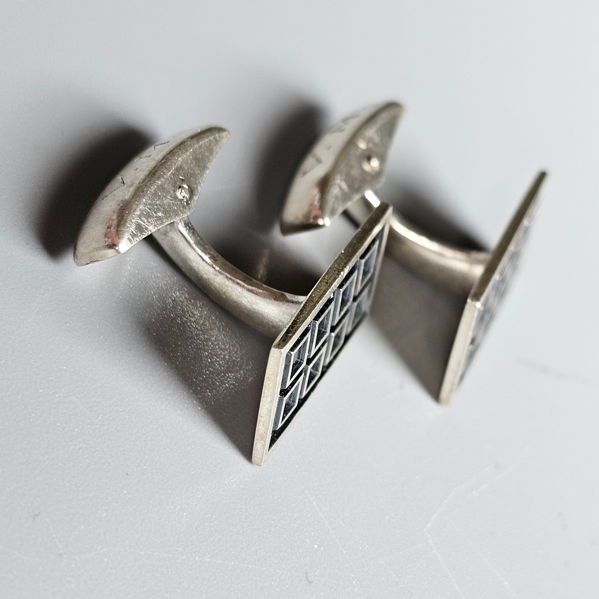 Pair of silver cufflinks with geometric patterned square faces.